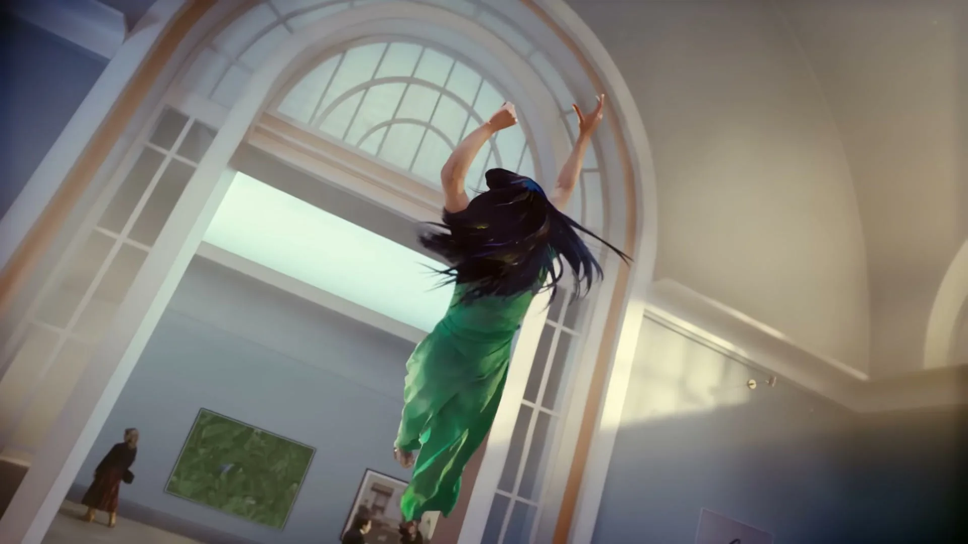 A woman in a green dress with dark hair floats upwards in a museum, arms raised, as if pulled by an unseen force.