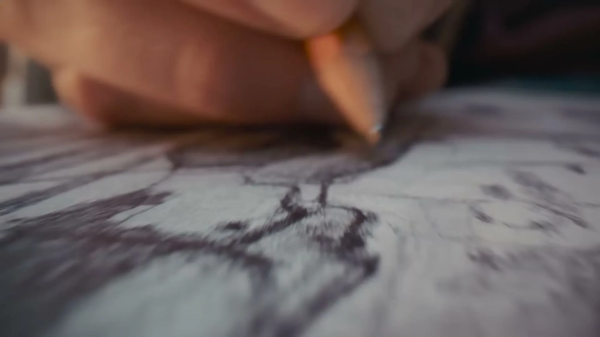 A person's hand holds a pencil, sketching details onto a piece of paper with an illustration, in a close-up shot.