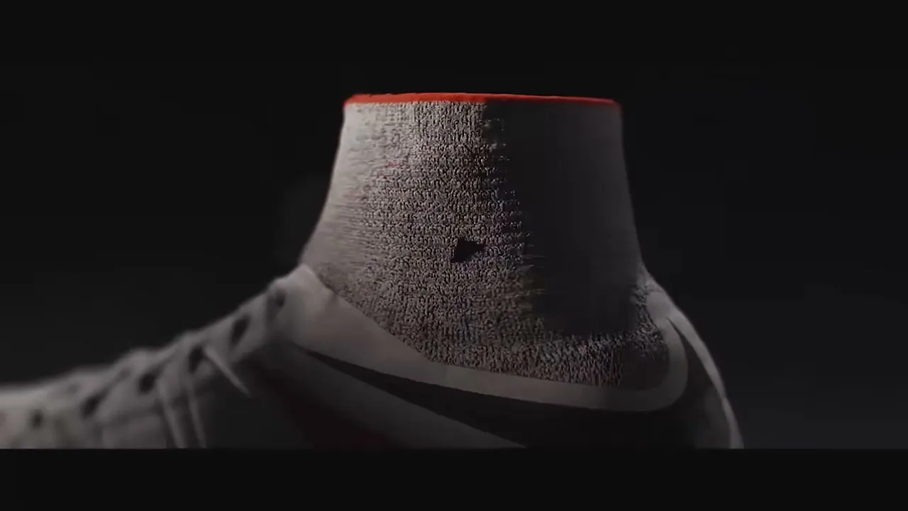 A close-up shot of a grey Nike Hypervenom soccer shoe with a red collar, as red particles appear and disappear on its surface.