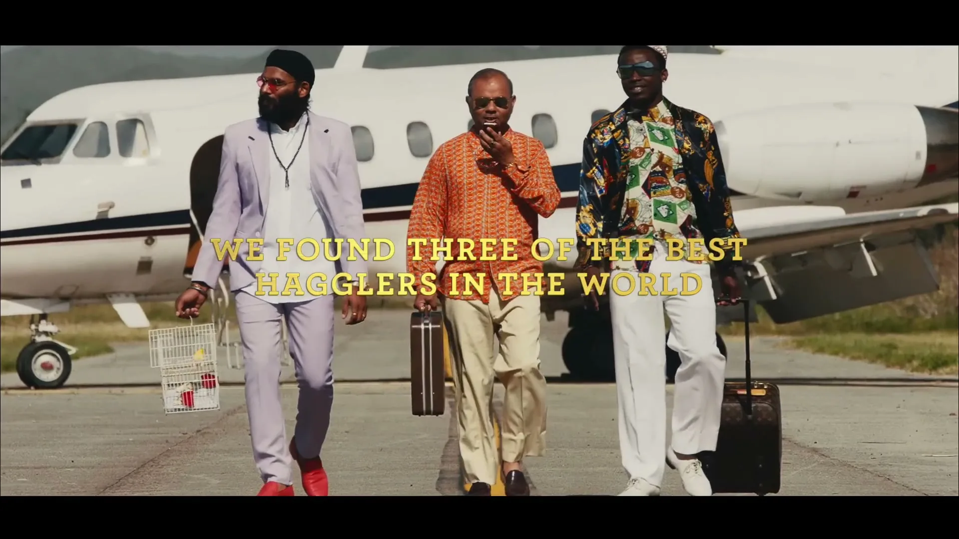 Three men in stylish, colorful outfits walk across an airport tarmac with a private jet in the background.