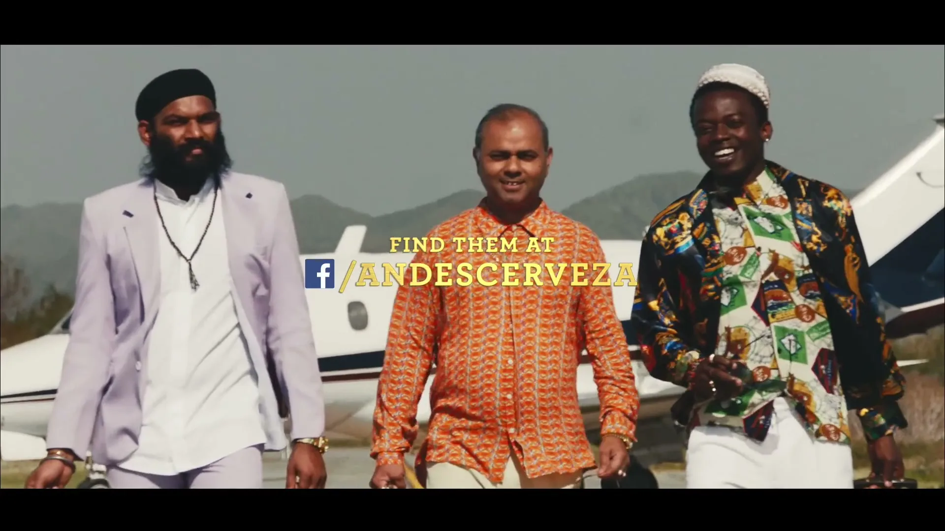 Three men in colorful outfits walk towards the camera on an airport tarmac with a private jet in the background, as text appears on screen.