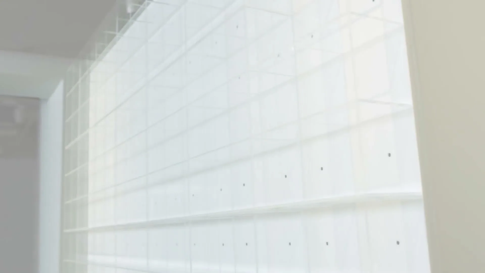 A white, translucent grid structure with small black dots is shown in a bright, minimalist interior space.
