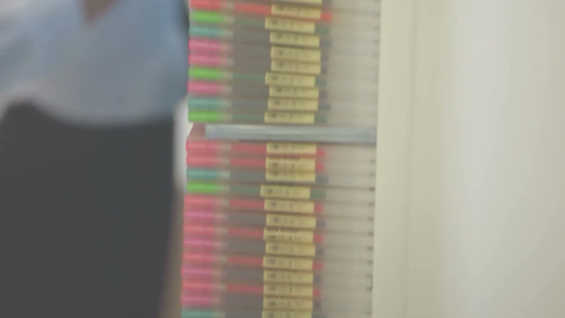 A person's hand reaches into a display of colorful pens, selecting one from the organized rows in a store.