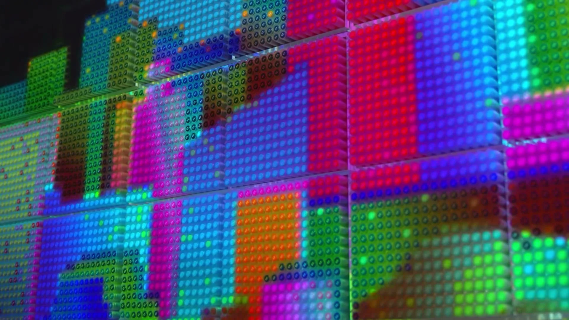A wall of colorful Muji pens creates a pixelated display, showcasing vibrant patterns and abstract designs in a studio setting.