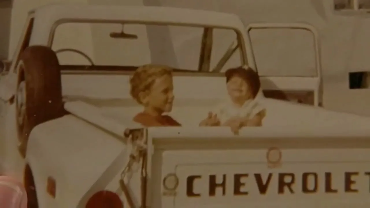 Two young children are seen laughing and playing in the back of a white Chevrolet pickup truck, captured in an old photograph.