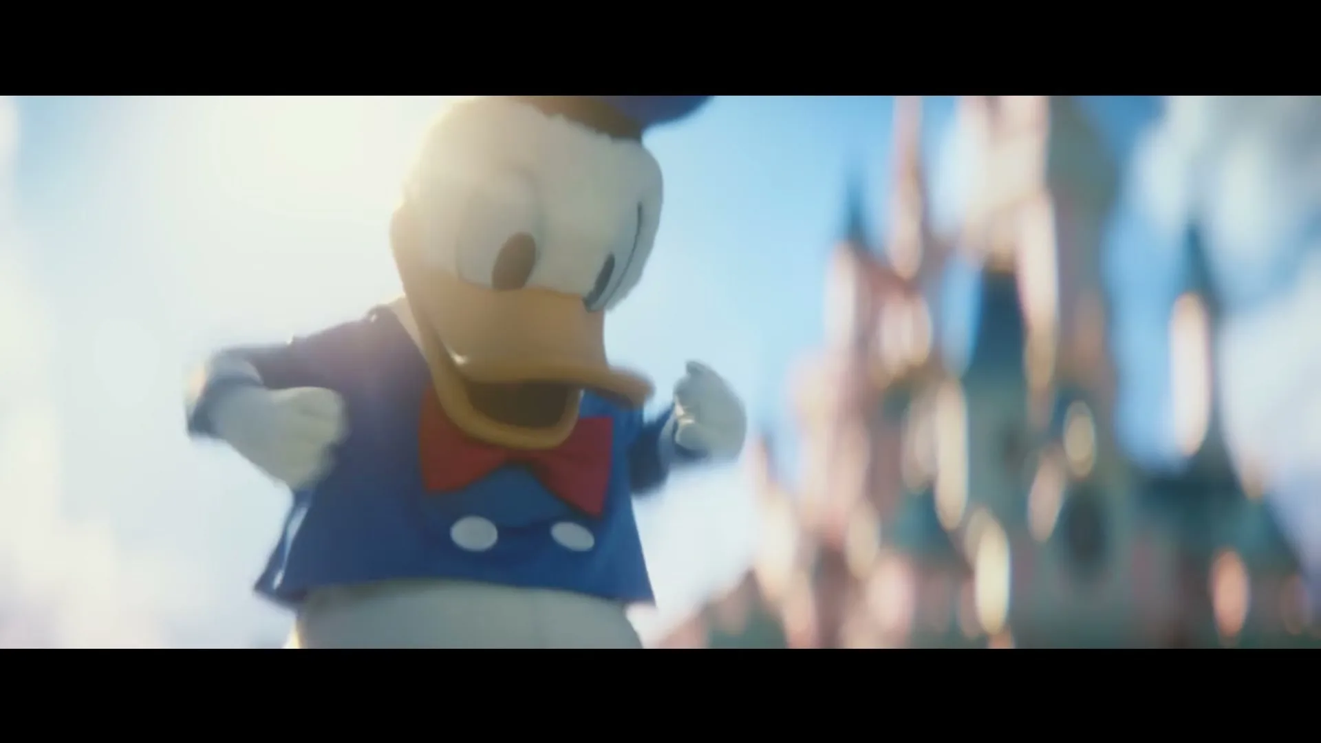 Donald Duck, in his classic sailor suit, looks down then opens his arms wide, with a blurred castle in the background.