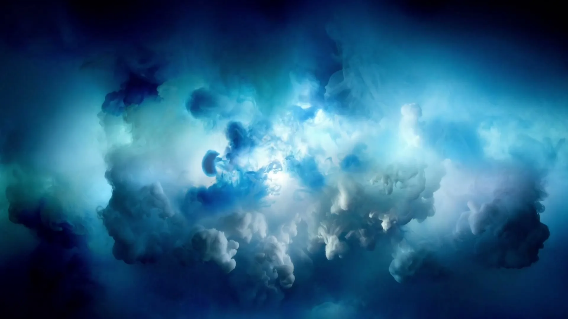 A dynamic shot of blue and white smoke or clouds swirling and expanding against a dark background, creating an abstract, ethereal visual.