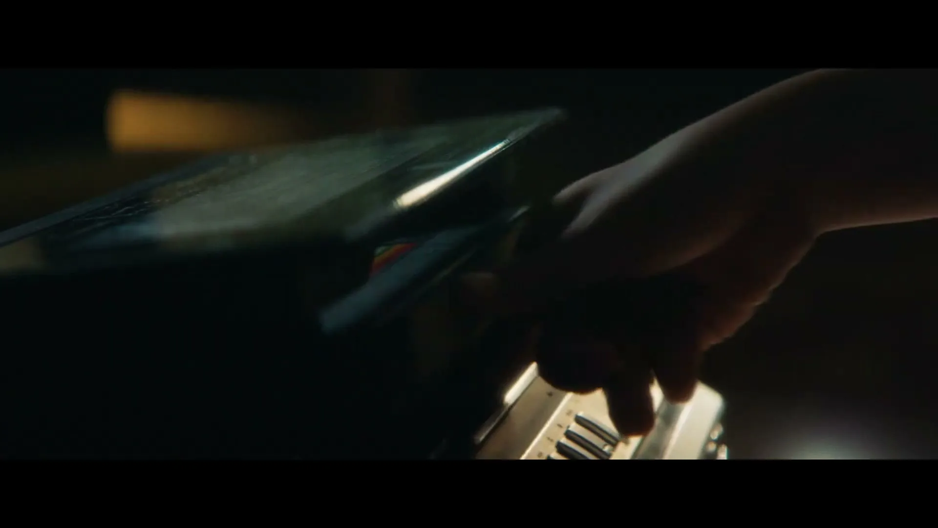 A person's hand is seen in a medium closeup, operating a vintage camera in a dimly lit interior setting.