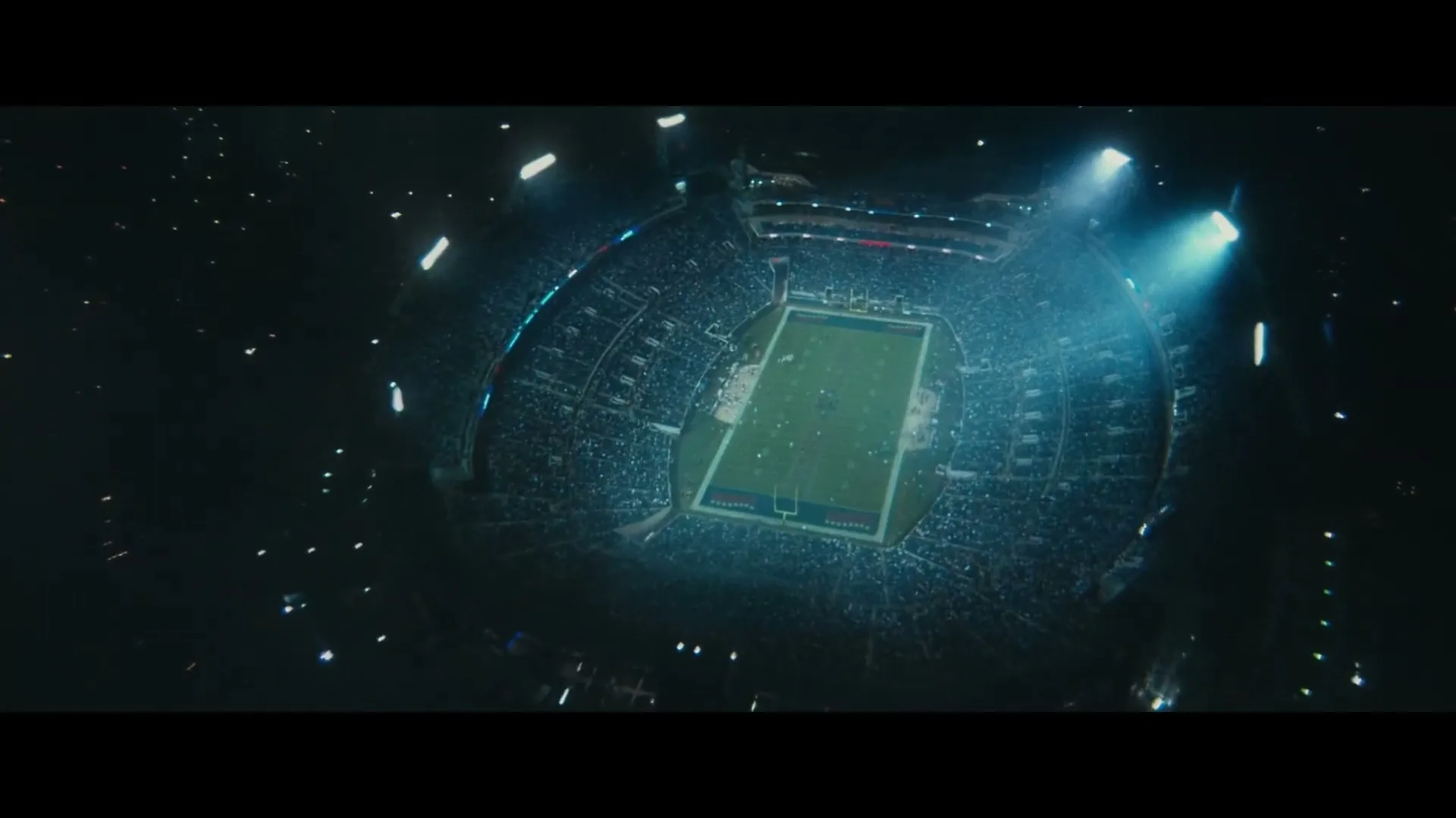 An aerial view of a packed football stadium at night, with bright lights illuminating the field and stands.