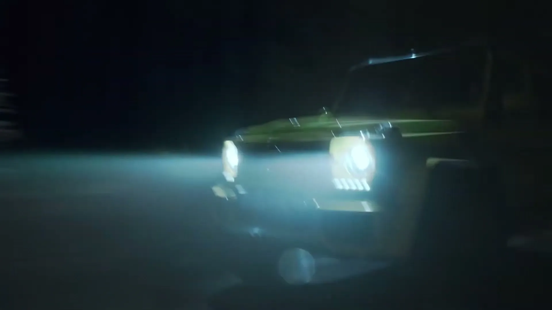 A bright yellow Mercedes-Benz G-Class drives through a dark, foggy night, its headlights cutting through the mist.