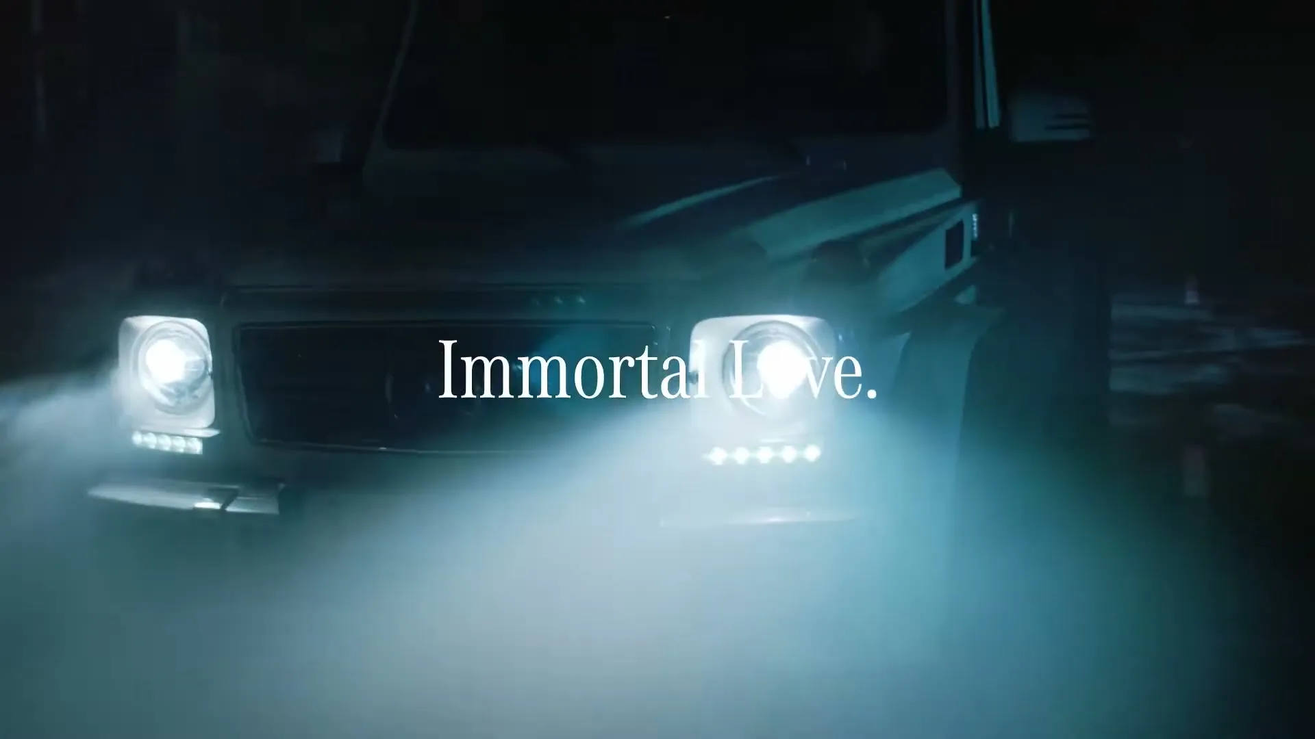 A white Mercedes-Benz G-Class SUV with its headlights on, emerges from fog at night, with the text "Immortal Love" superimposed.