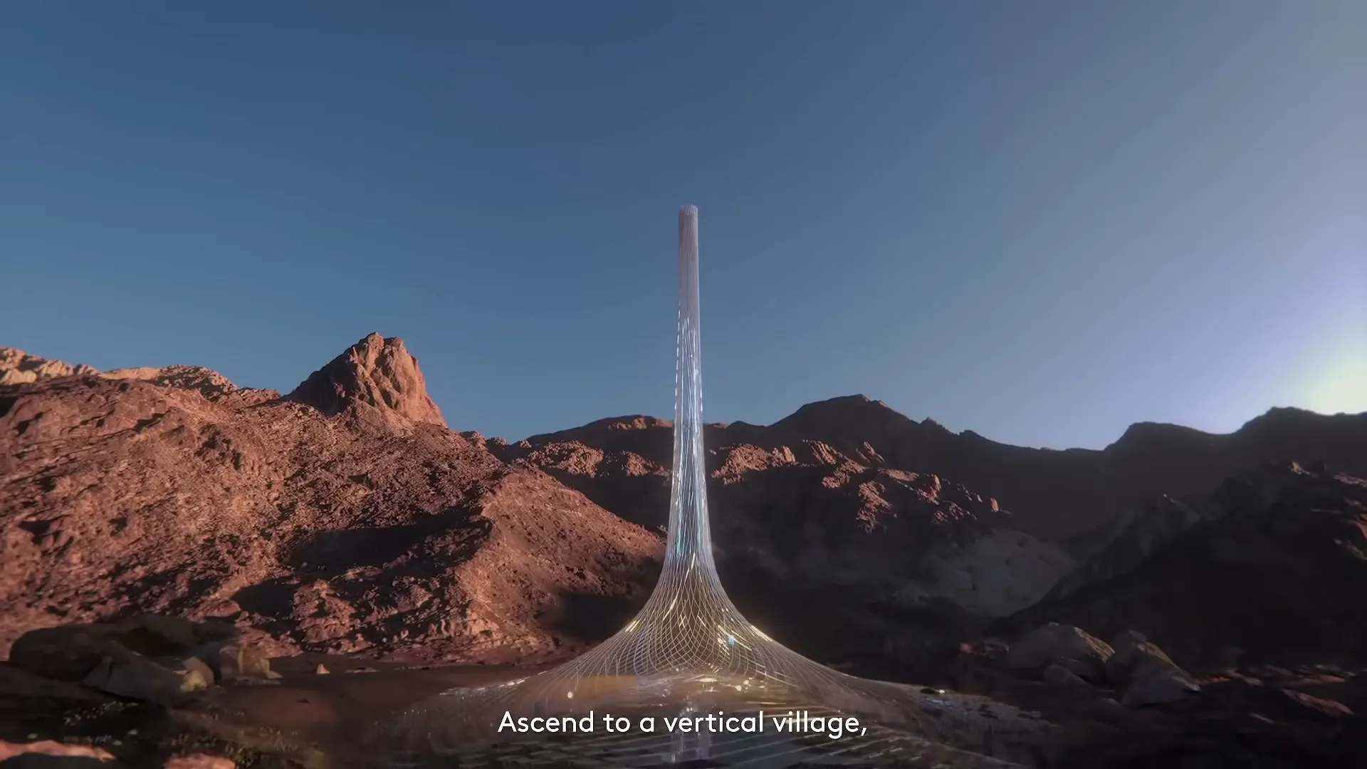 A futuristic, tall, slender building with a wide base stands in a desert valley surrounded by rocky mountains under a clear blue sky.