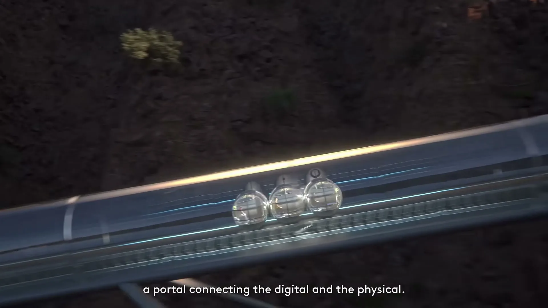 A futuristic train with spherical cars travels along a transparent track built into a rocky mountain landscape.
