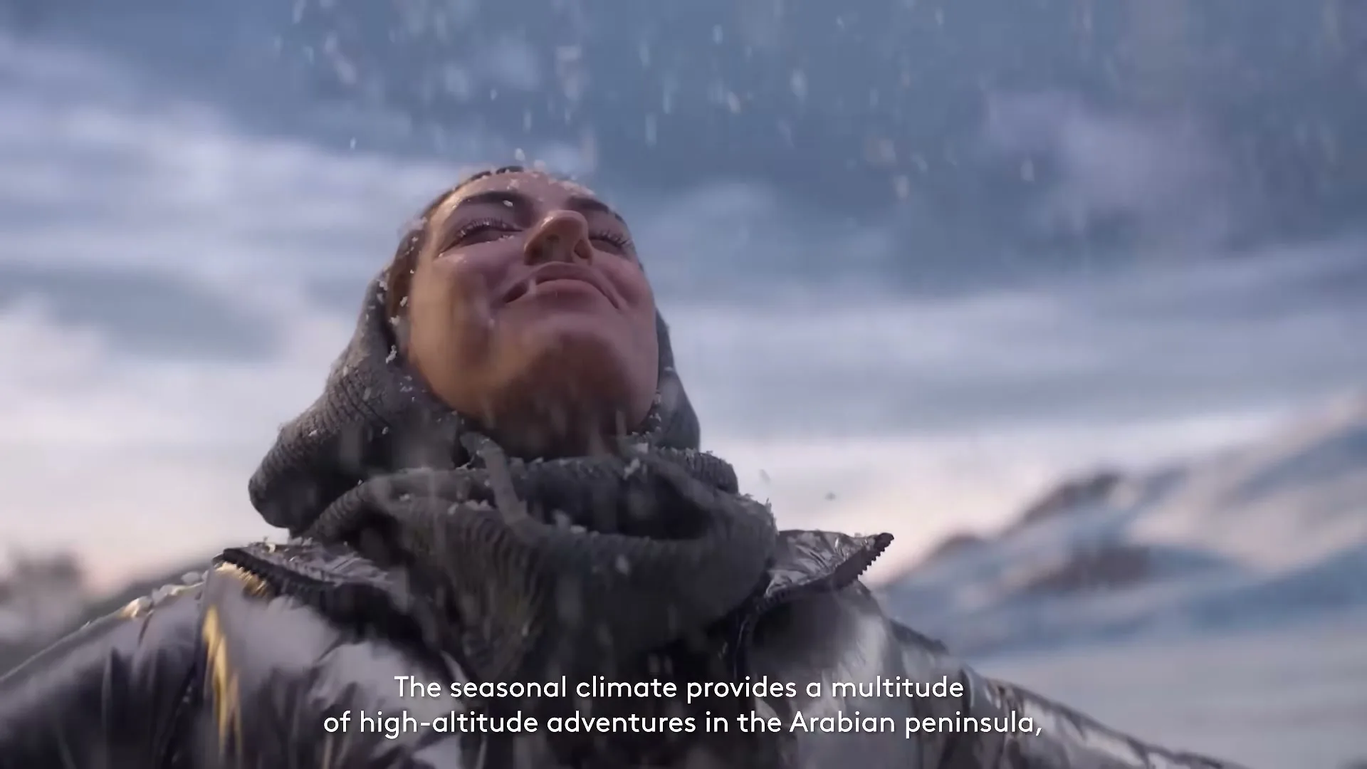 A woman in a silver puffer jacket and grey scarf stands with her arms outstretched, eyes closed, as snow falls on her face in a snowy mountain landscape.