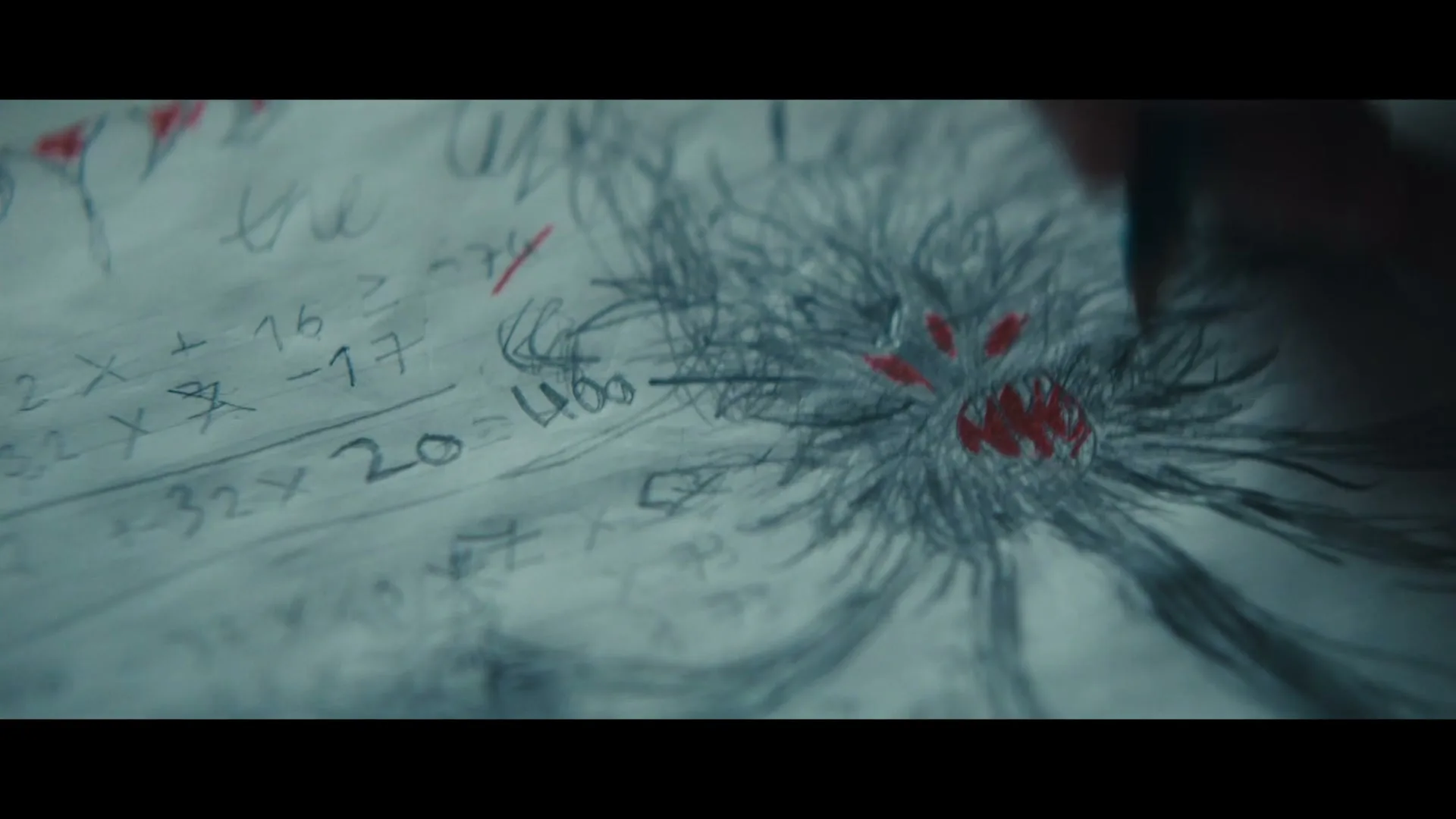 A child's hand draws a scary monster with red eyes and mouth on a piece of paper with math equations in a dimly lit room.