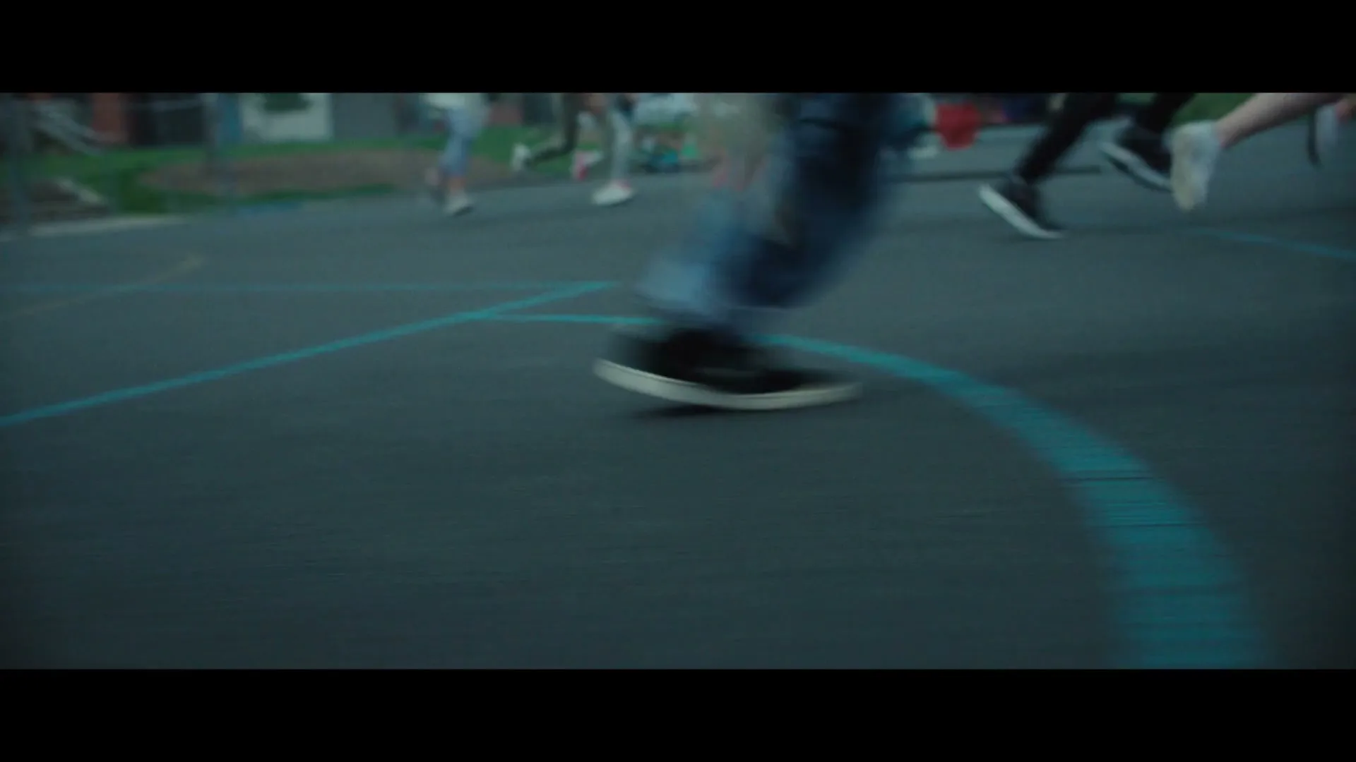 A low-angle shot of children's legs and feet running on a dark blue playground with light blue lines.