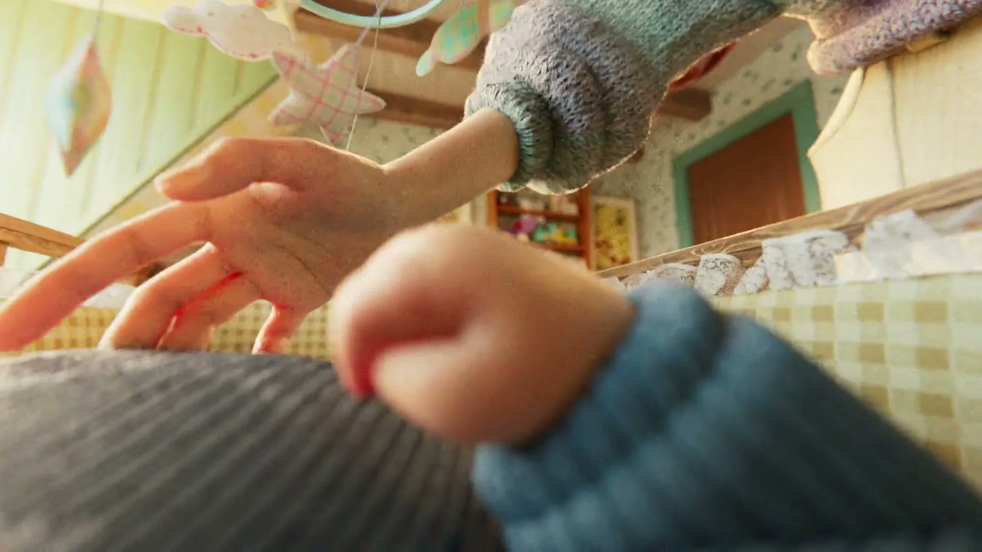A baby in a crib reaches up towards a mobile, then a mother leans over the crib and smiles at the baby.