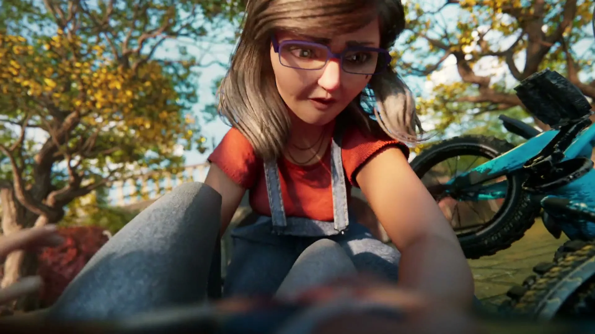 A young woman with glasses and overalls helps a person who has fallen off their bike in a park.