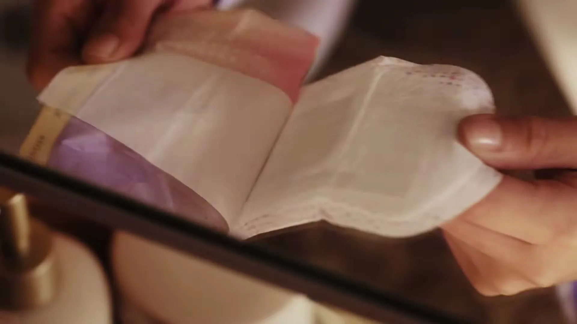 A person's hands, wearing striped pajamas, peel open a sanitary pad over a bathroom counter.