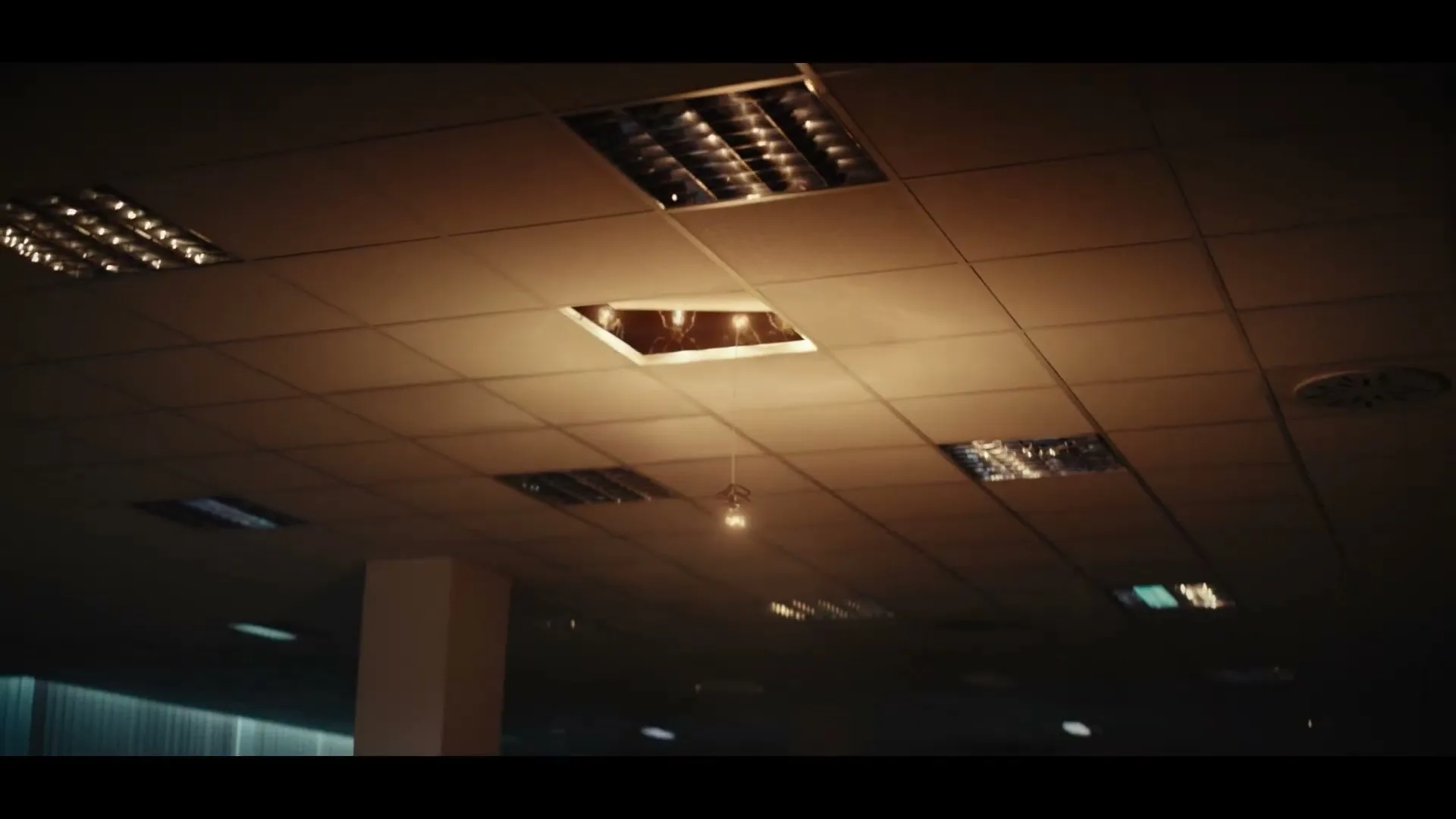 A single lightbulb hangs from a broken ceiling tile in a dimly lit, empty office, slowly lowering into view.