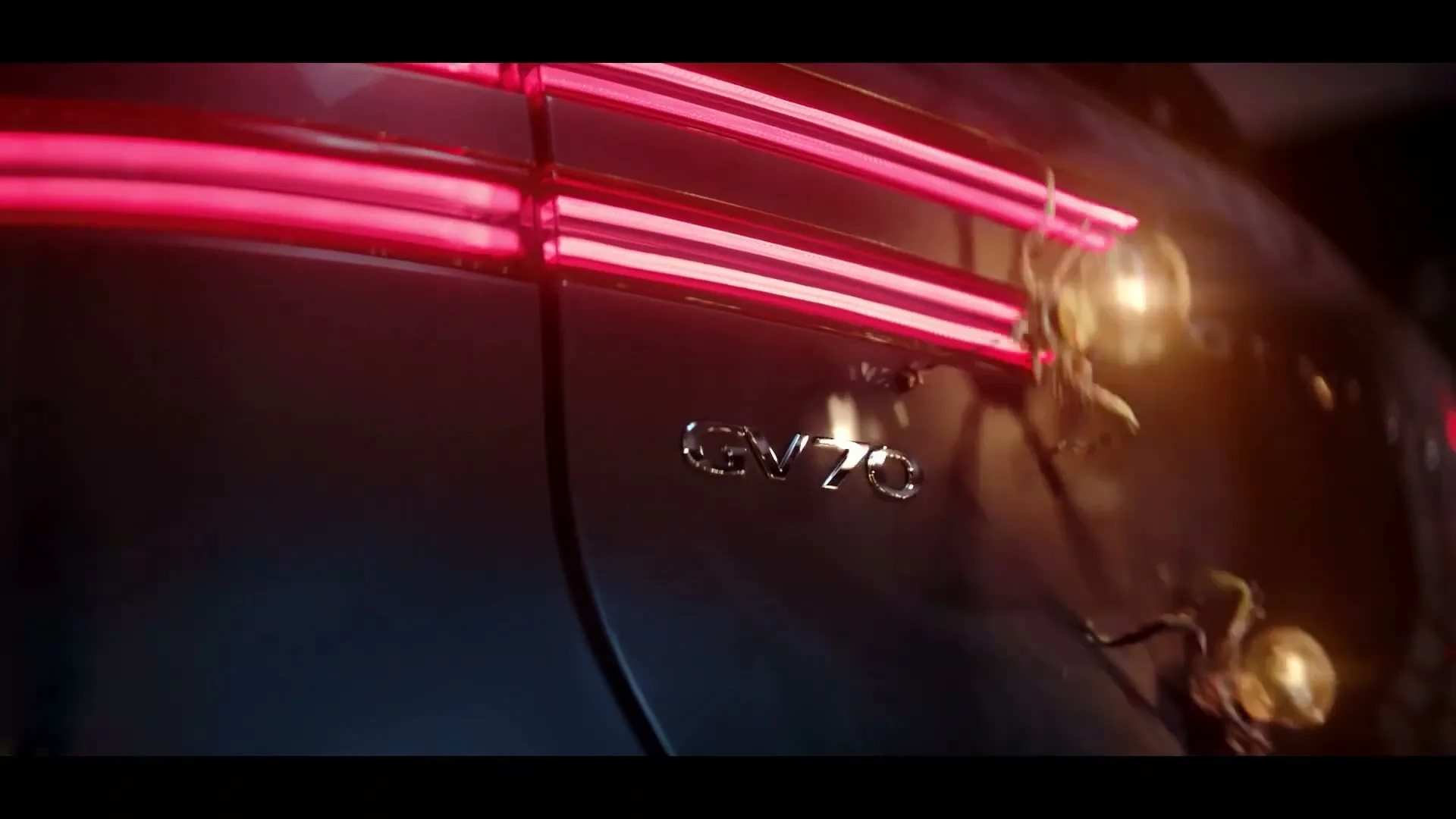 The rear of a dark Genesis GV70 car is shown with its bright red taillights on, as small, glowing, insect-like creatures crawl across its surface.