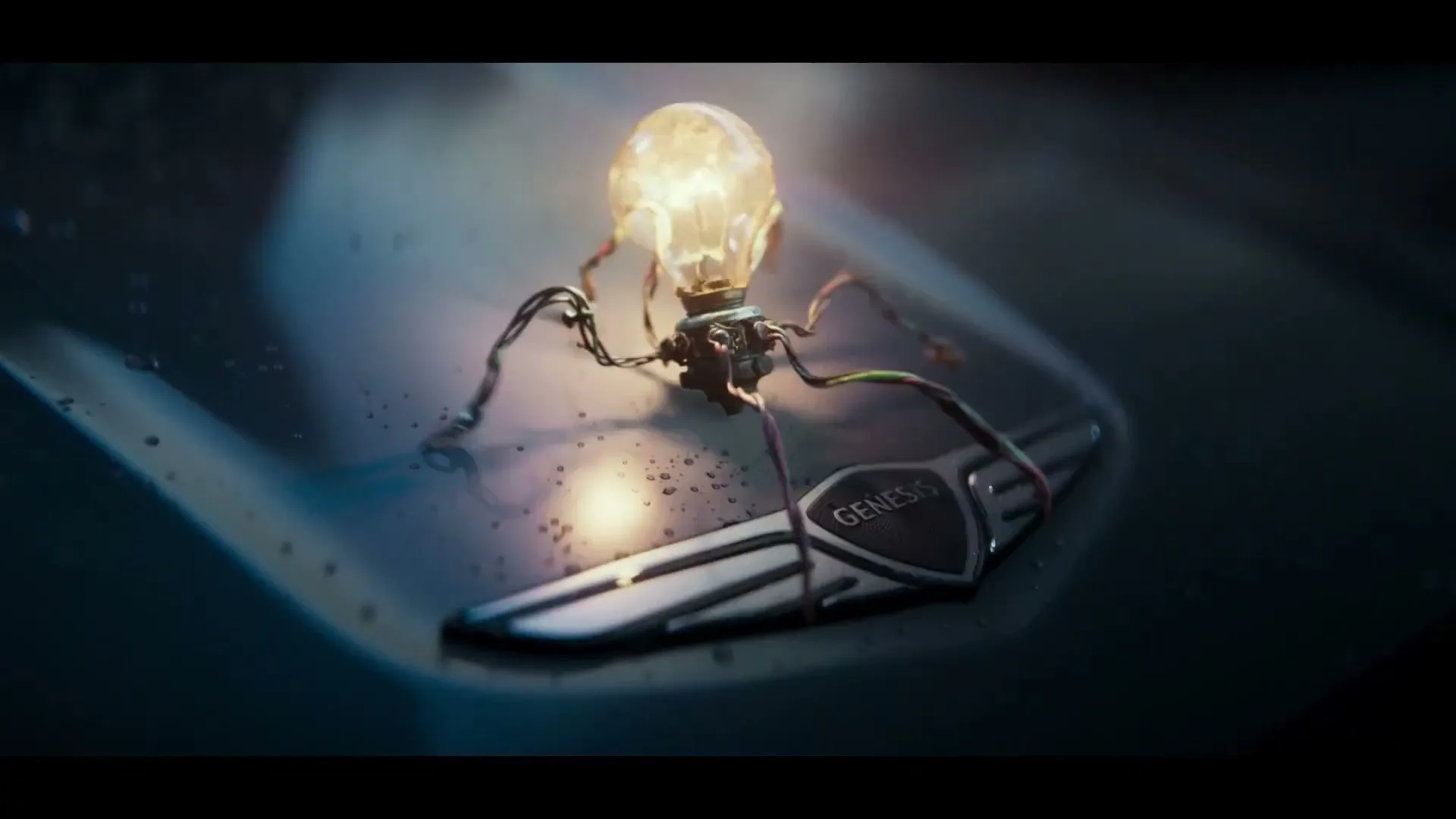 A glowing lightbulb-creature with wire legs stands on a wet, dark car hood next to a shiny Genesis logo, then disappears.