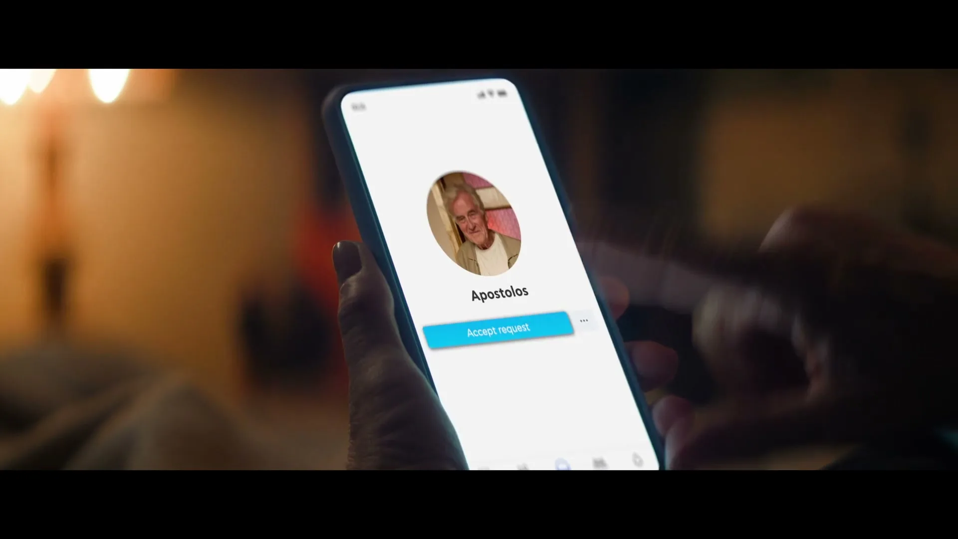 A woman's hand holds a smartphone displaying a social media profile for "Apostolos" with his photo, as her finger taps "Accept request" in a cozy, dimly lit room.