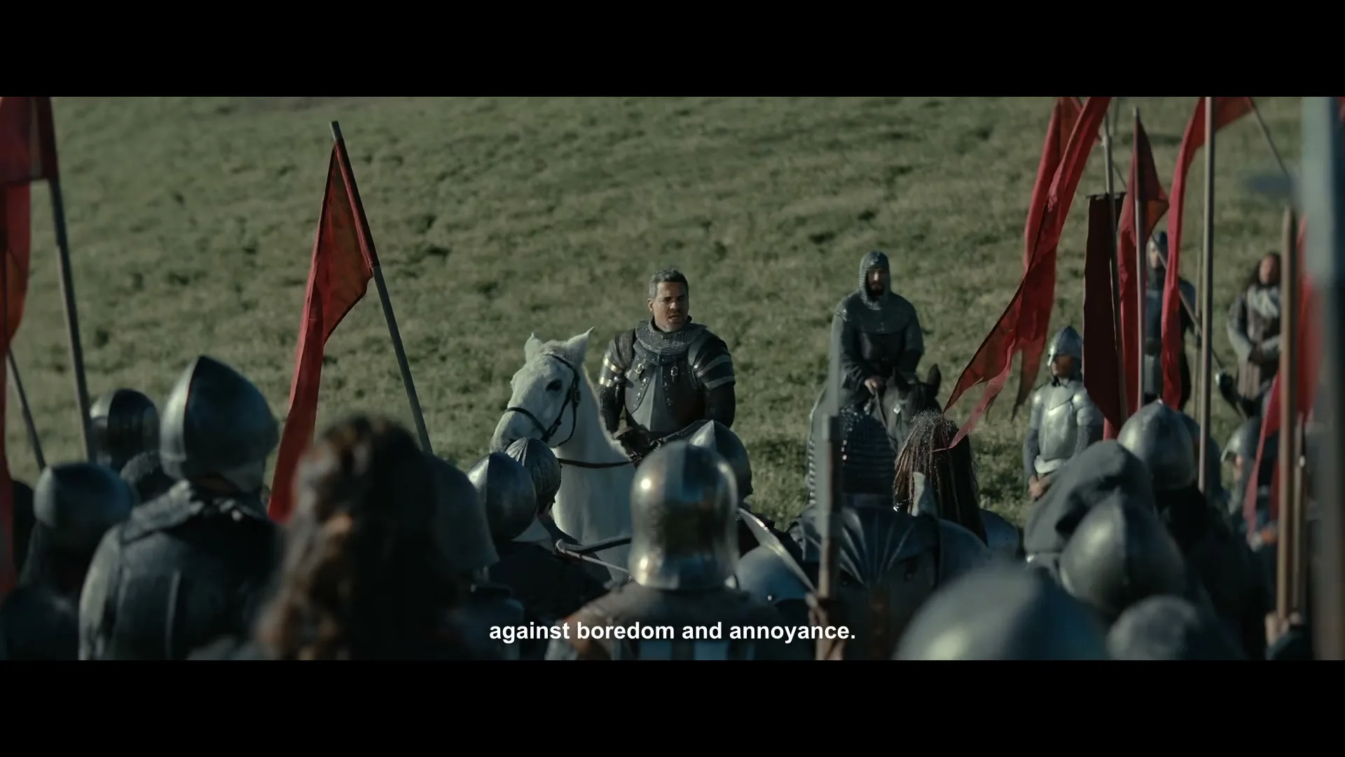 A medieval general on a white horse addresses his army of knights and soldiers, who are gathered on a grassy battlefield under a bright sky.