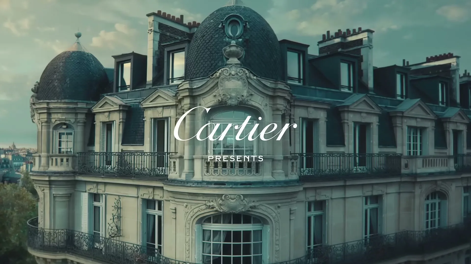 An ornate, classic Parisian building with a domed roof is shown from an aerial perspective, with the Cartier logo and "PRESENTS" text overlaid.