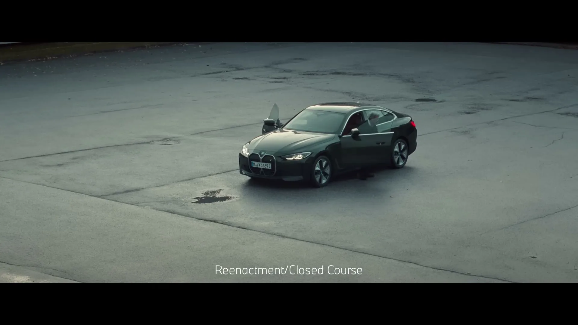 Two older men with white hair, dressed in dark suits, exit a dark green BMW car on a large, empty asphalt lot under an overcast sky.