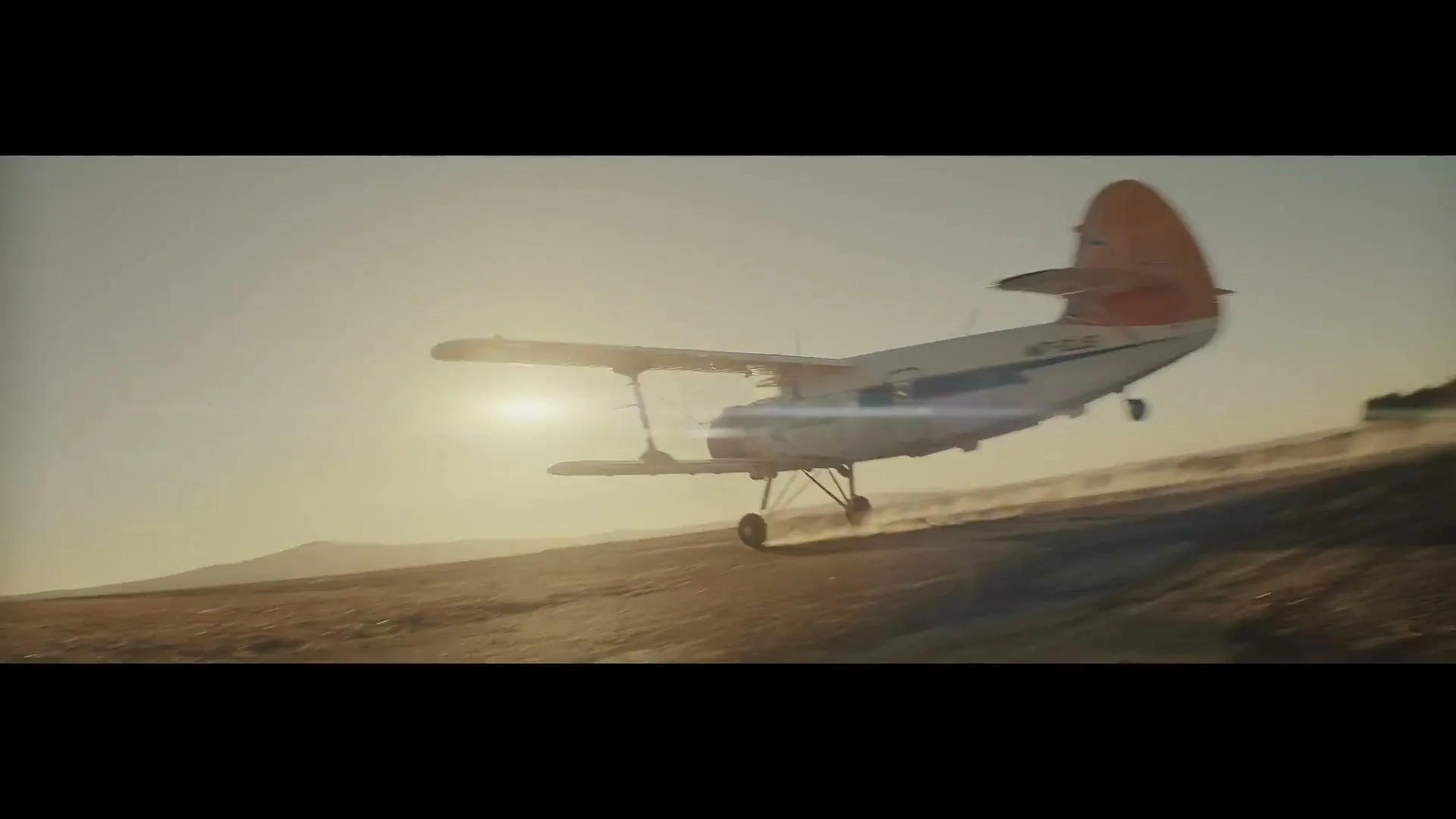 A biplane takes off from a dusty, arid landscape under a bright sky, kicking up dirt as it ascends.