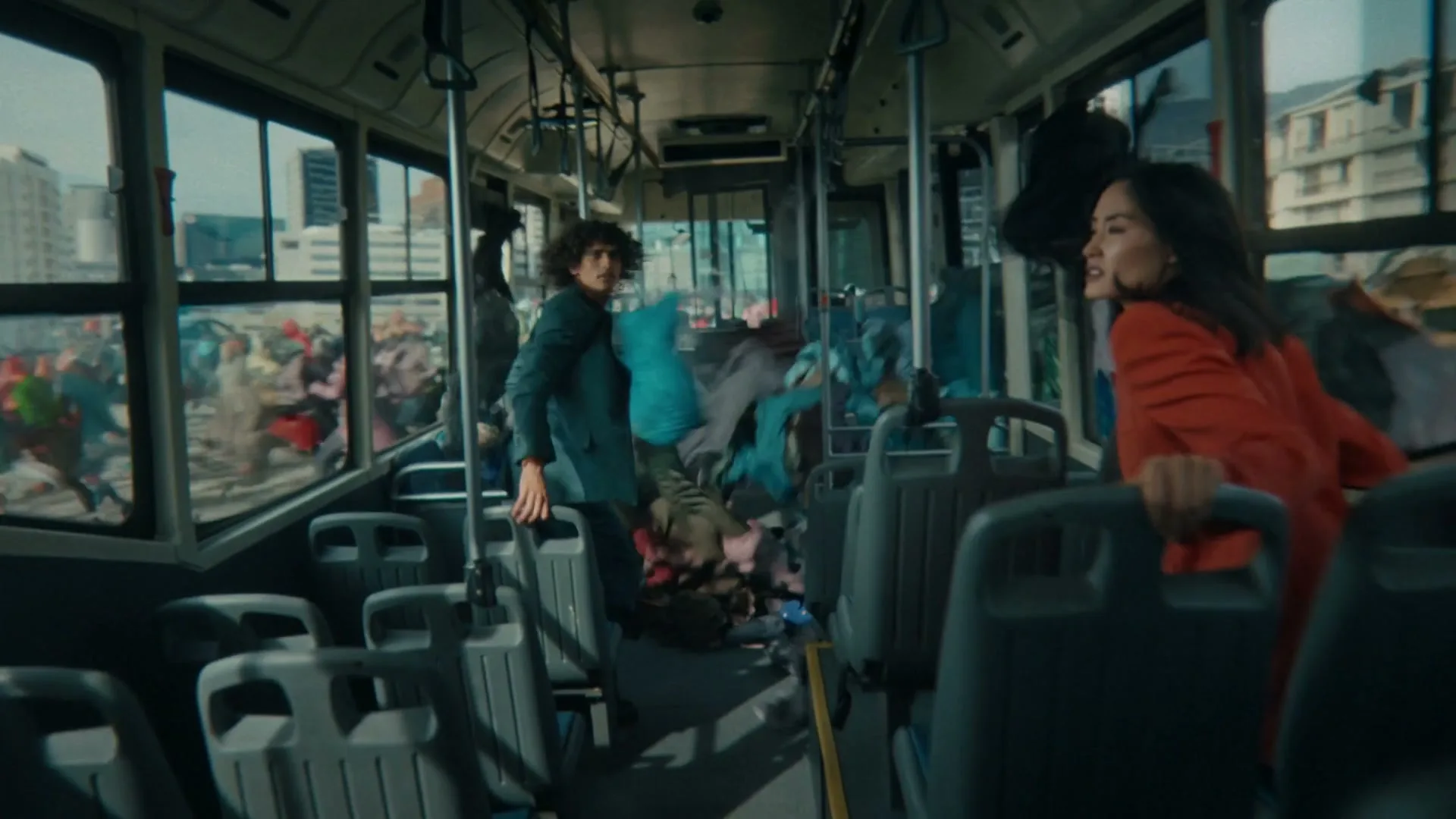 Two people on a bus look out the window at a street filled with discarded clothing, as more clothes fly into the bus.