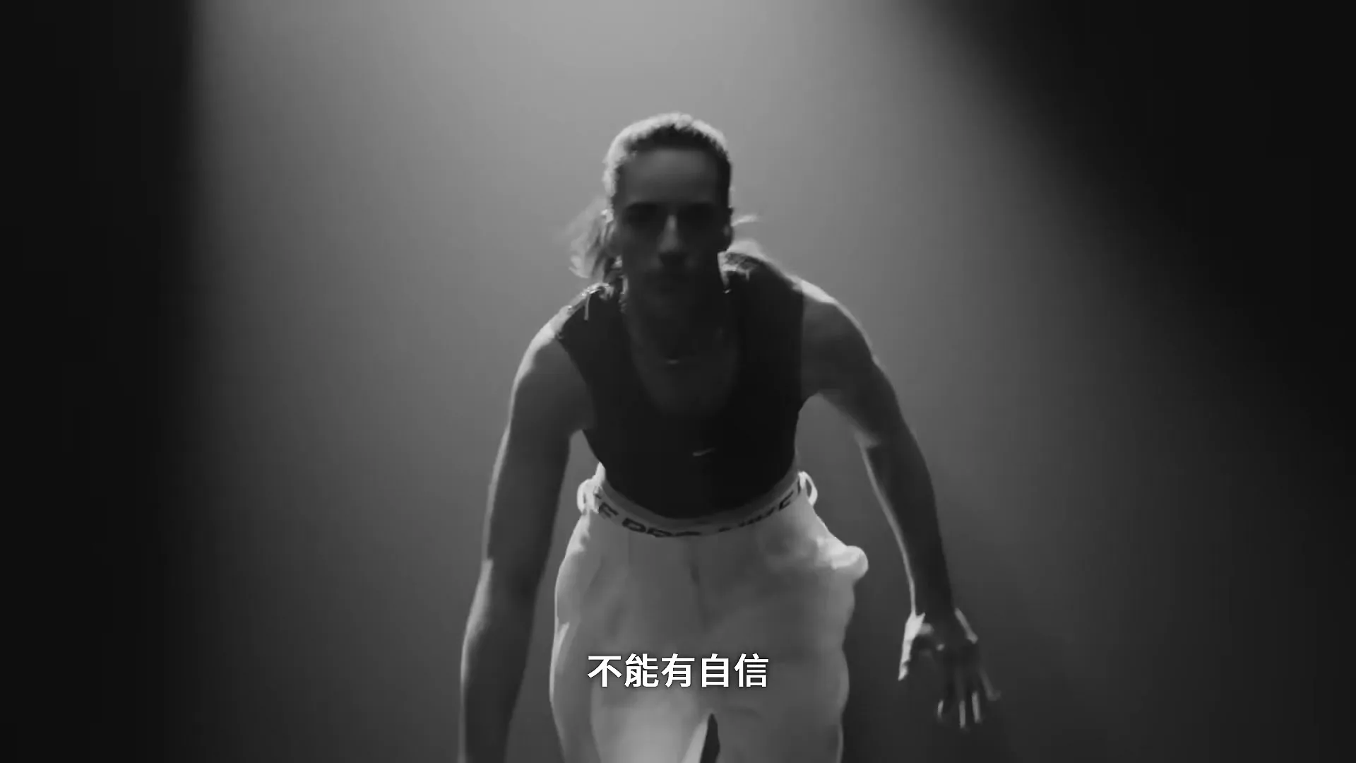A female basketball player in athletic wear dribbles a basketball in a spotlight against a dark background.