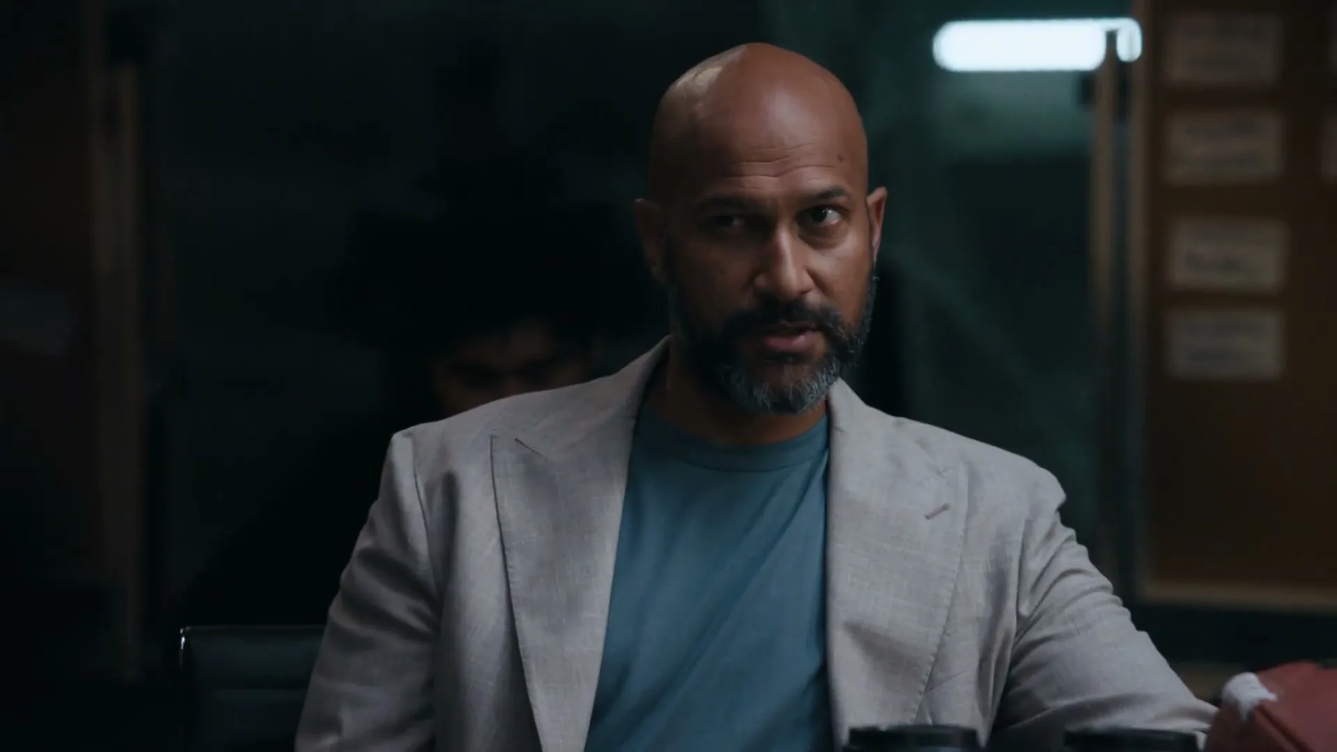 Keegan-Michael Key, a bald man with a beard, wearing a light blazer and blue t-shirt, sits at a table and speaks in an office.