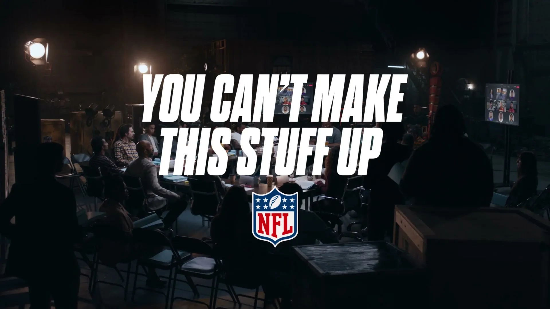 A group of people are gathered in a dimly lit room, with a large screen displaying "YOU CAN'T MAKE THIS STUFF UP" and the NFL logo.