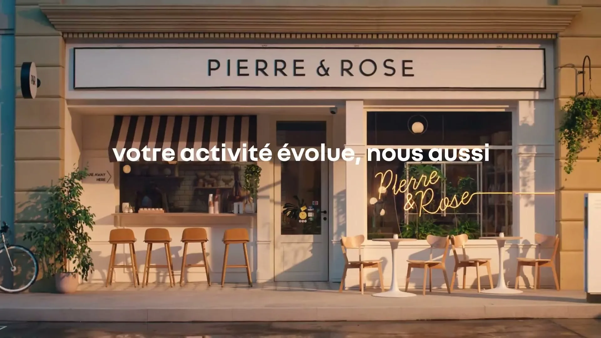 A wide shot of a charming cafe with outdoor seating and a black and white striped awning, with text overlayed on the screen.
