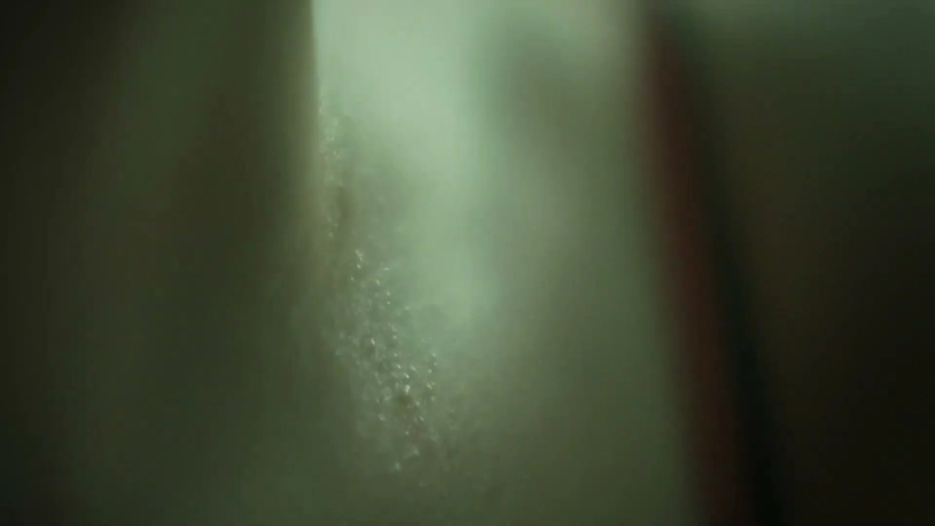 A blurry, extreme close-up shot of water droplets on a surface, possibly a shower wall, with soft light filtering through.