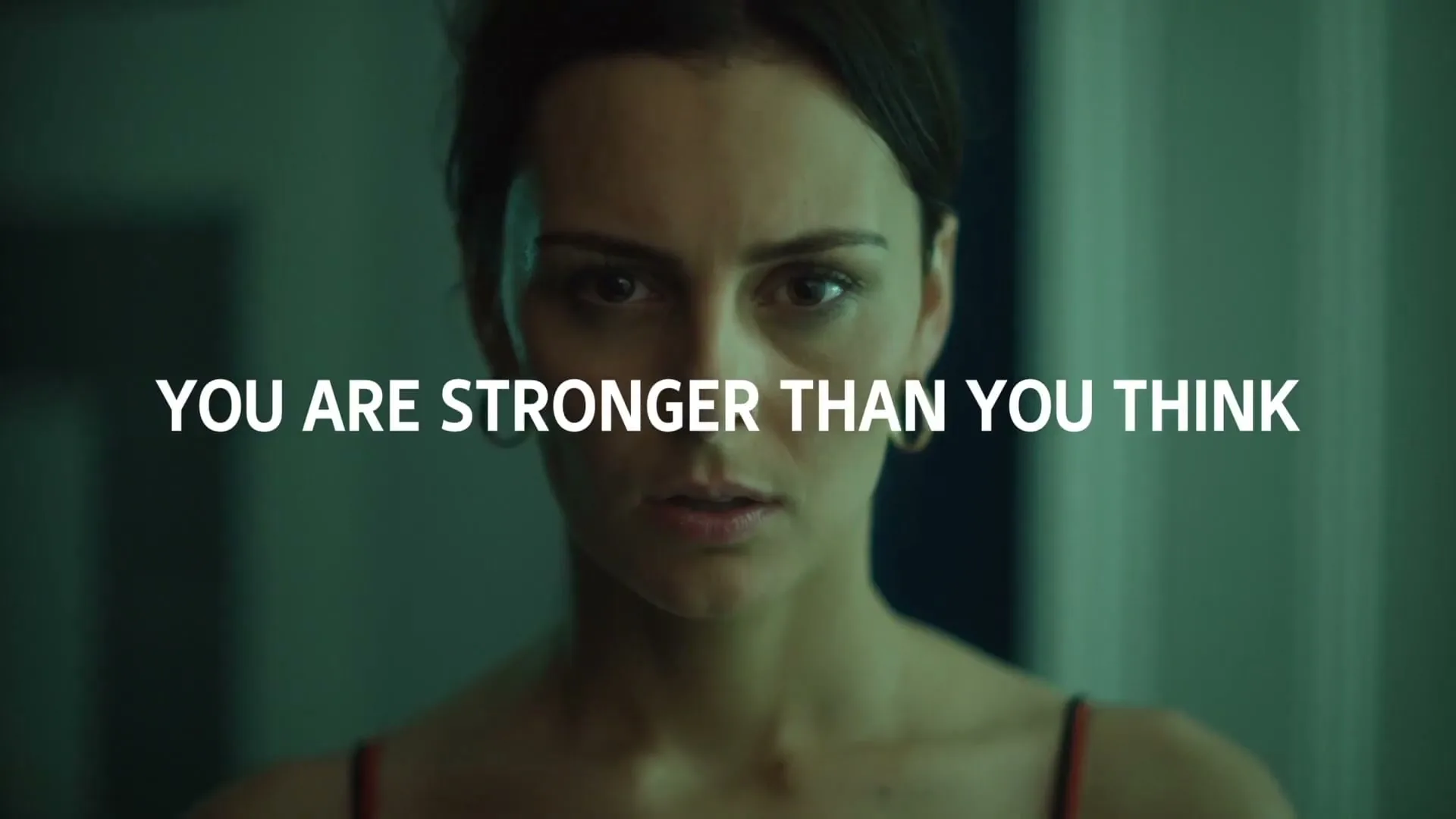 A woman with dark hair and a serious expression looks directly at the camera, with white text overlaid on the screen.