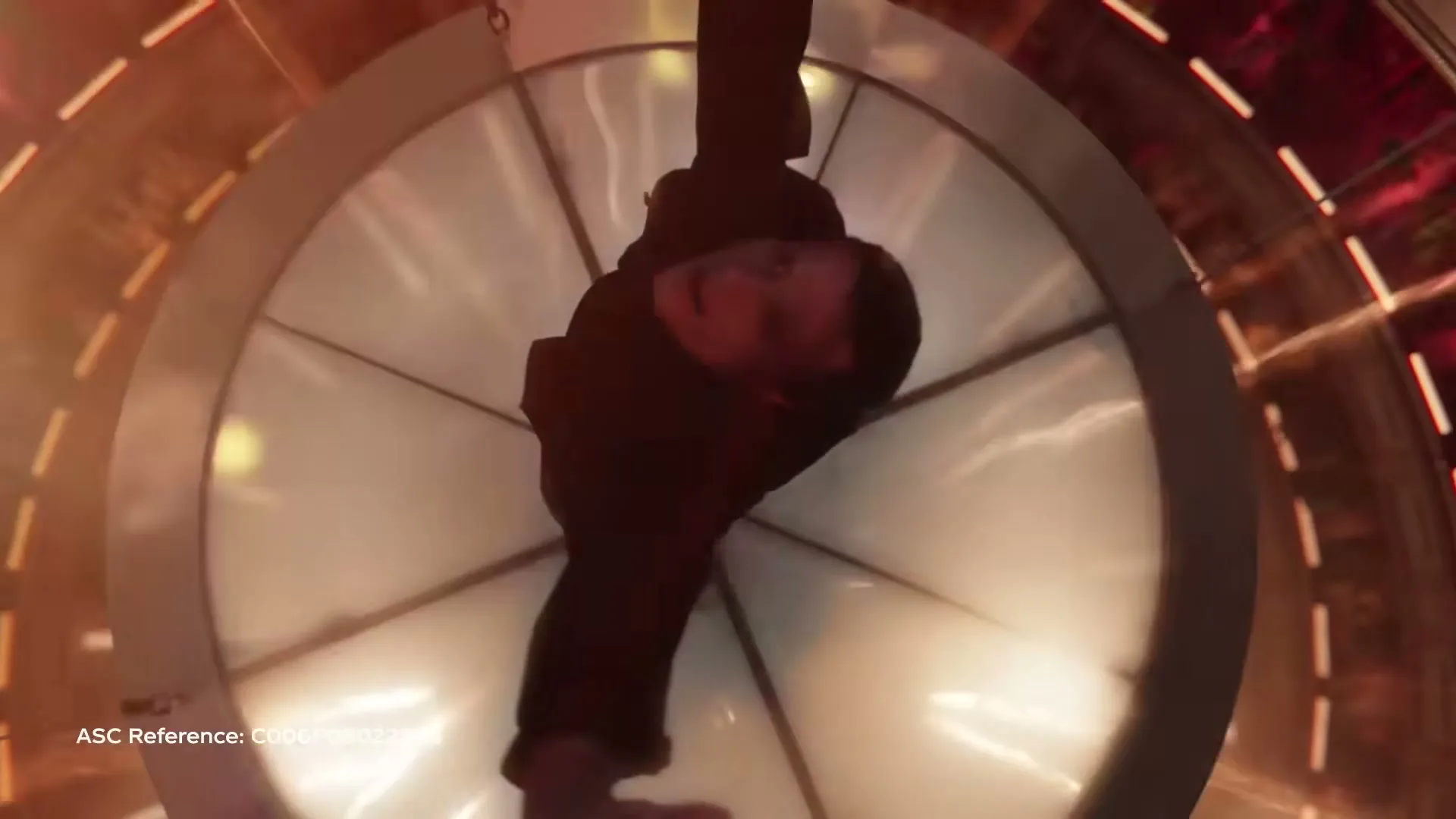 A young man in a black jacket hangs upside down, reaching out his hand, in a brightly lit, futuristic circular tunnel.