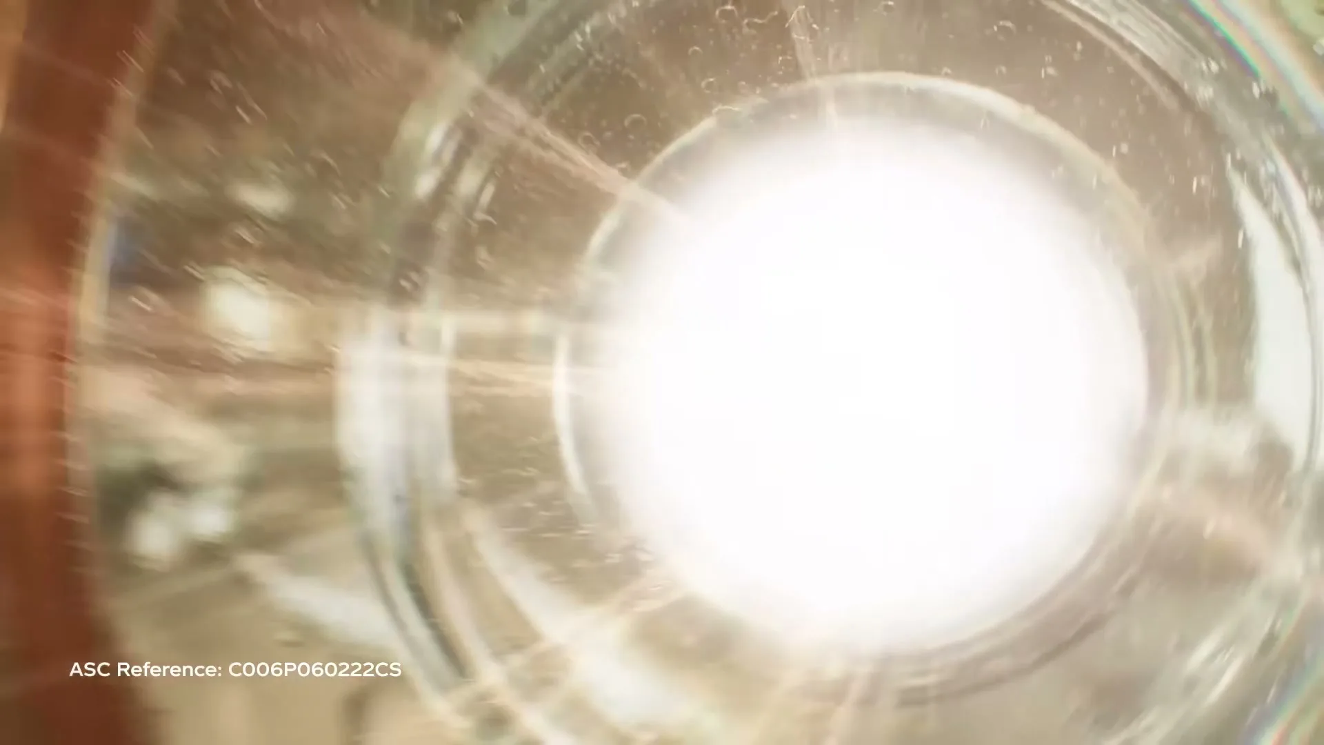 A bright light shines through a glass bottle, then white pellets fall into the bottle, creating a fizzy effect.