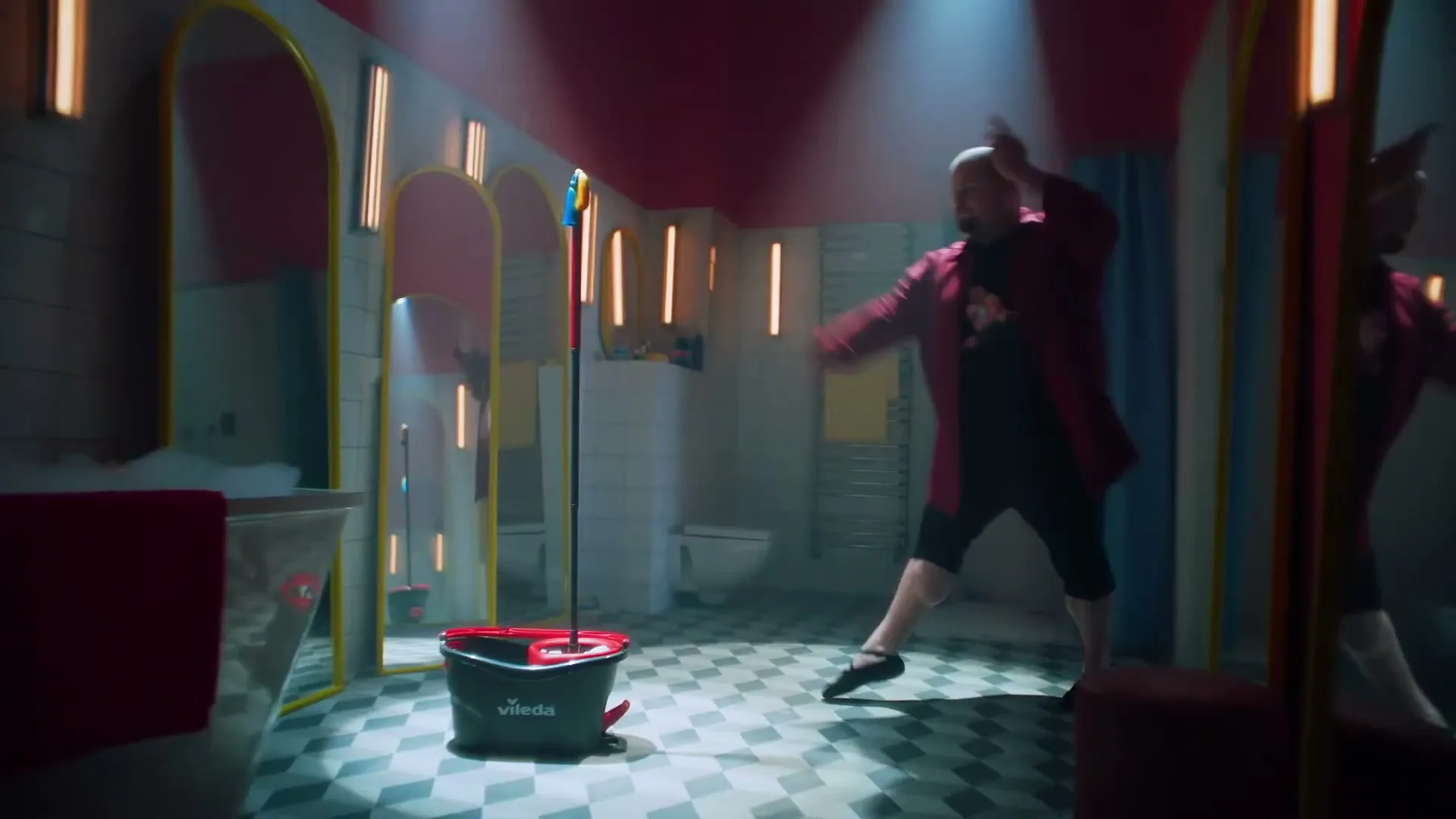A man in a red robe dances in a brightly lit bathroom with a Vileda mop and bucket in the foreground.