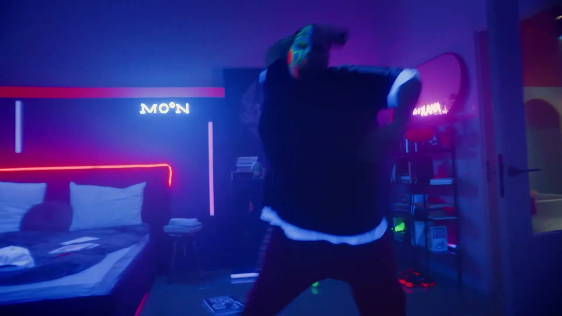 A person with face paint and a black shirt dances energetically in a neon-lit bedroom at night.