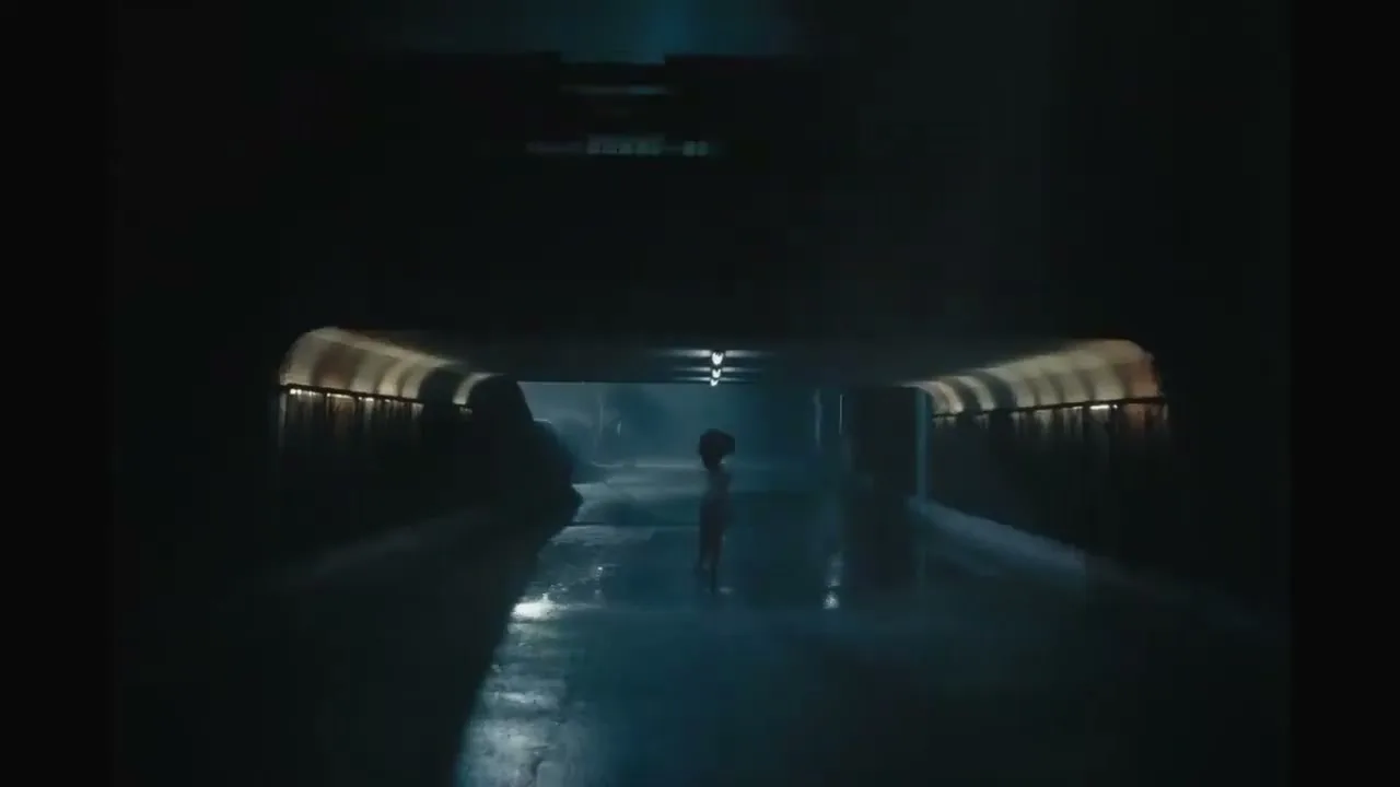 A young girl with curly hair stands in a dark, wet tunnel, illuminated by a distant light, looking small and isolated.