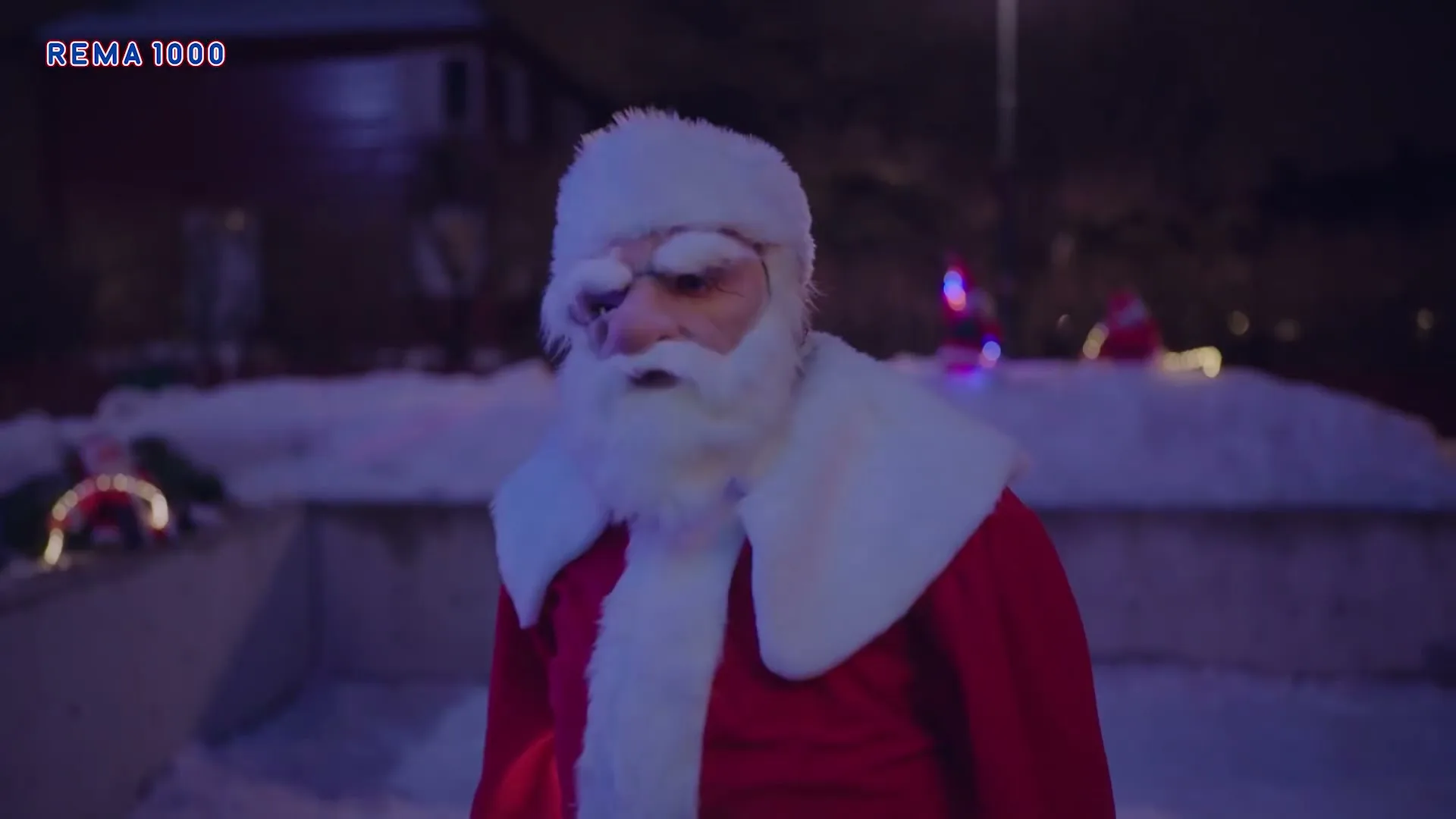 A man dressed as Santa Claus, with a frozen face and beard, stands outside in the snow at night.