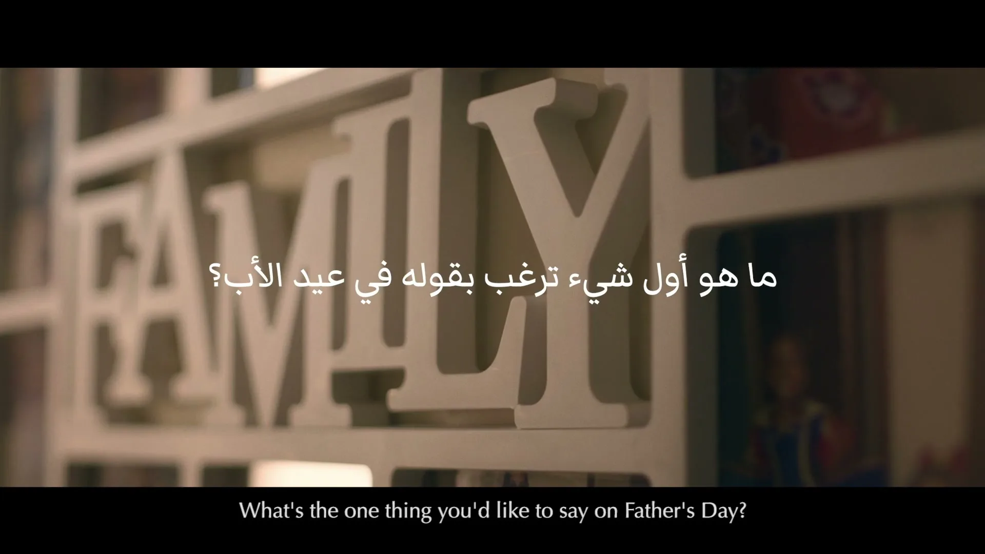 A close-up shot of a white wooden "FAMILY" sign with photo frames in the background, as text appears on screen.