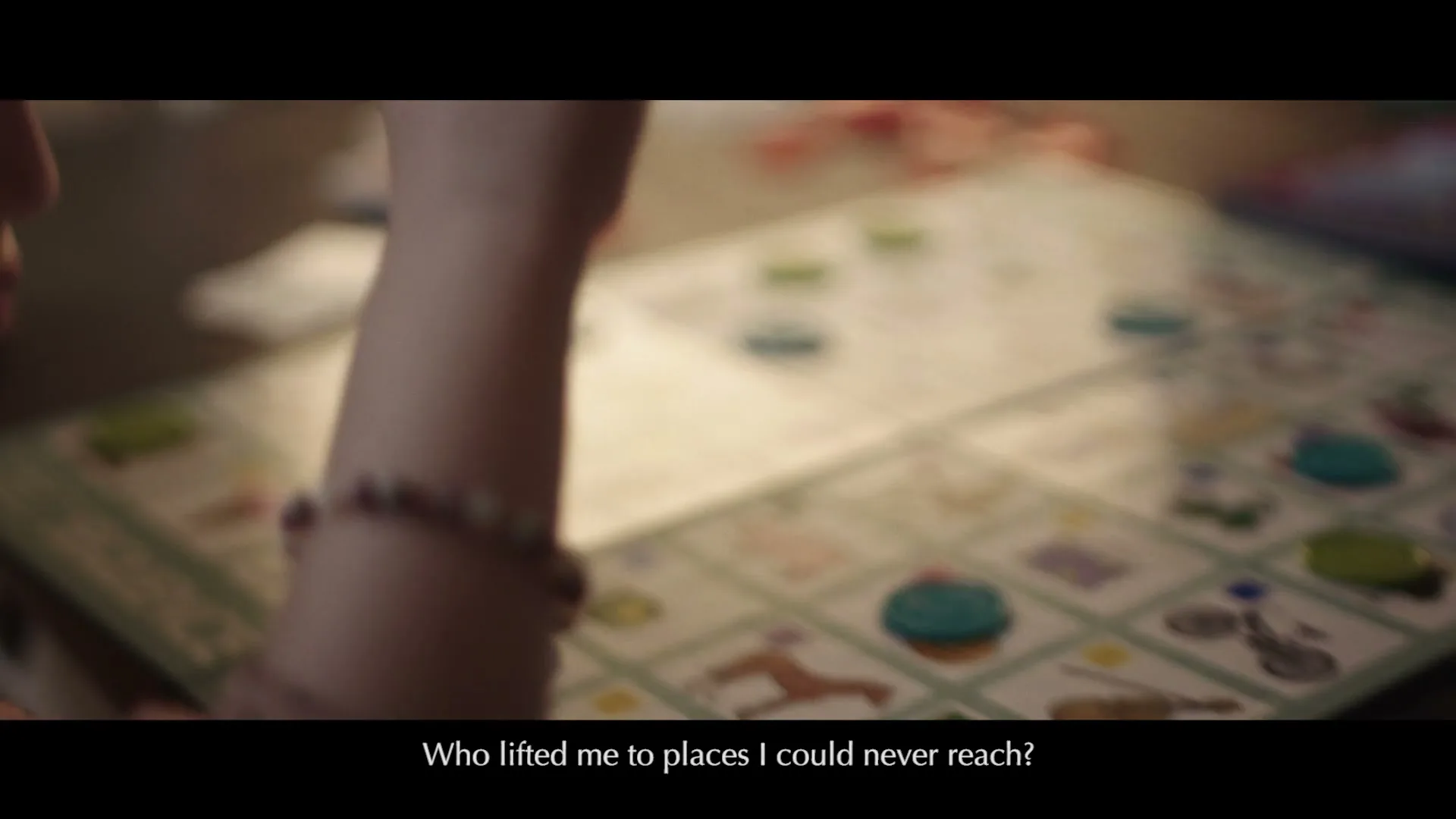A child's arm with a beaded bracelet reaches across a board game with colorful tokens on a wooden table, playing a game.