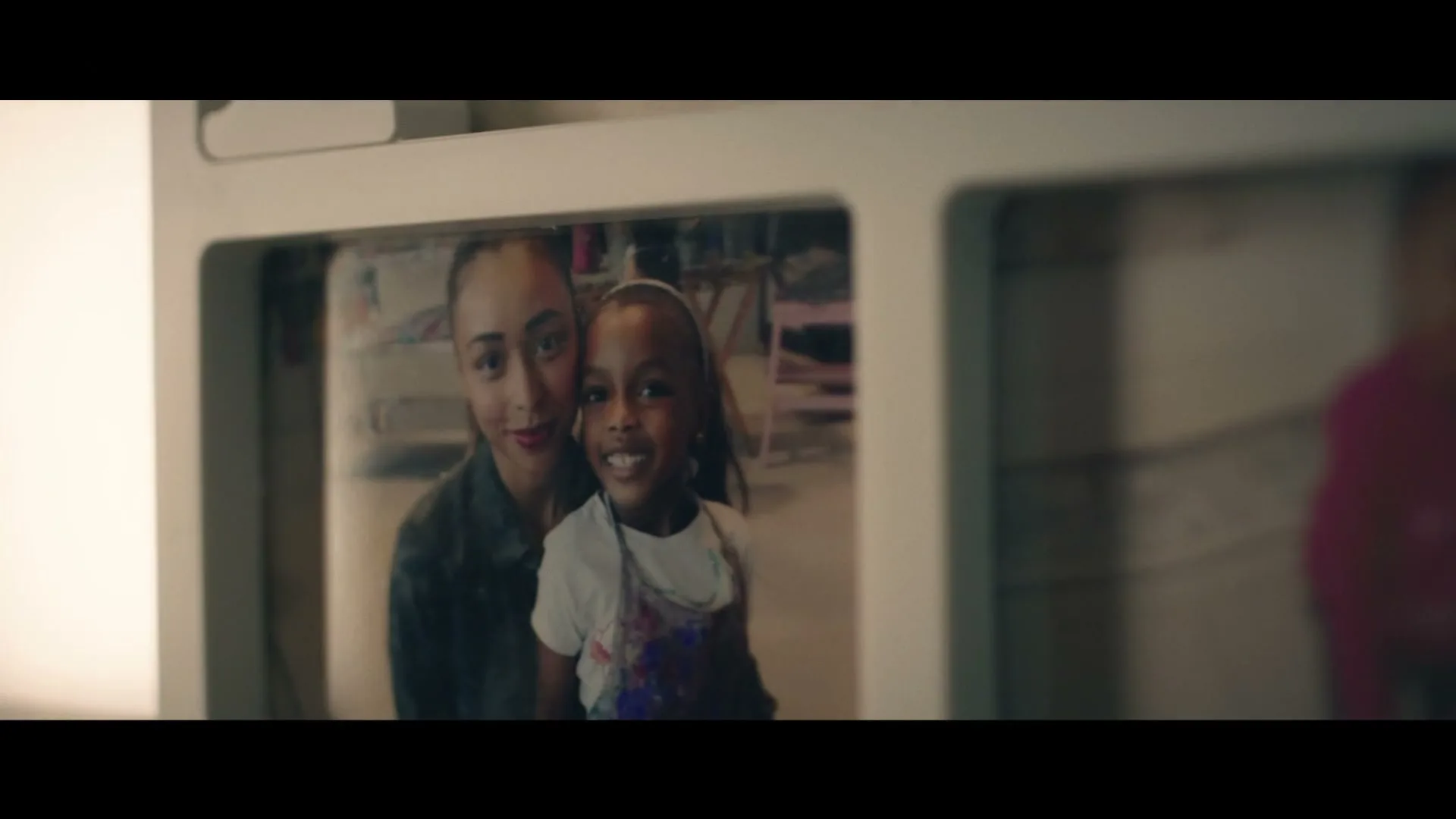 A close-up shot of a white photo frame, revealing a photo of a woman and a young girl smiling at the camera.