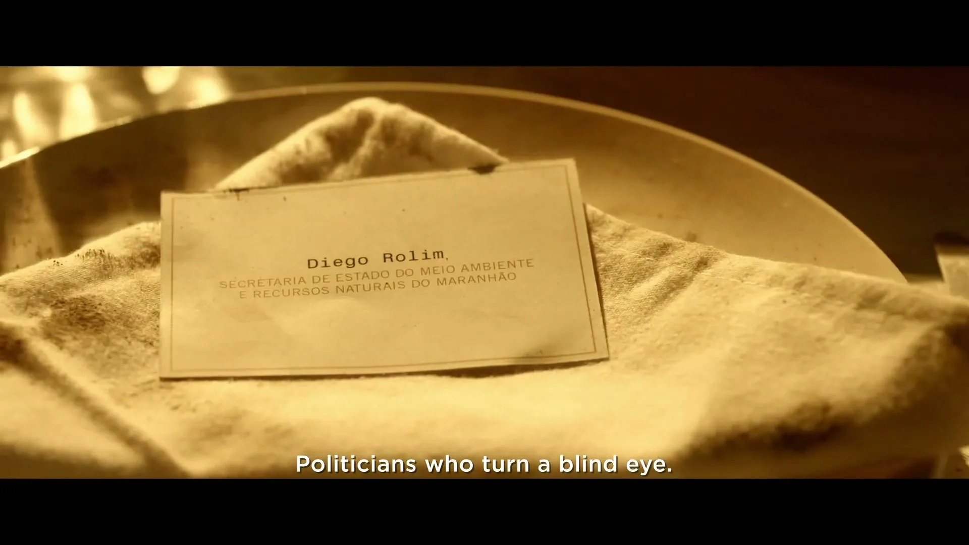 A business card for "Diego Rolim" from the "Secretaria de Estado do Meio Ambiente e Recursos Naturais do Maranhão" rests on a dirty cloth in a metal bowl.