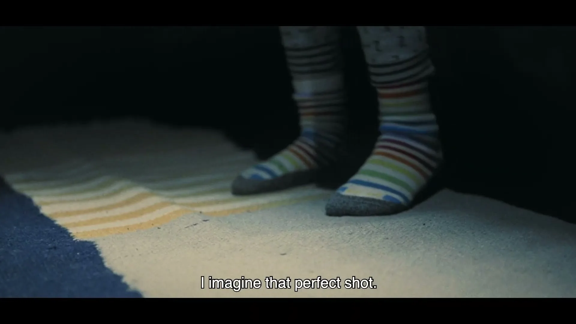 A child's feet in colorful striped socks step onto a rug in a dimly lit room, as if getting out of bed.