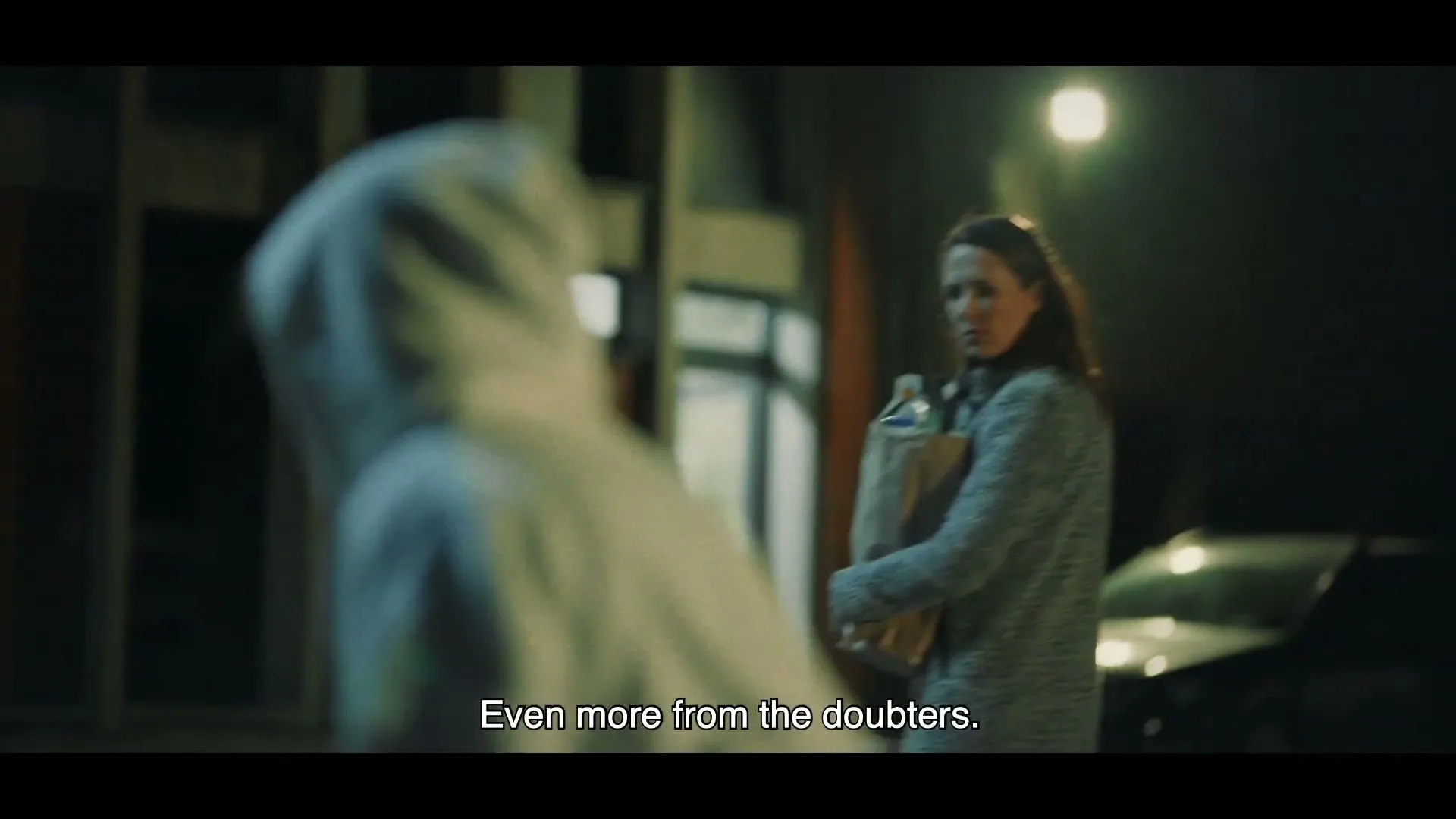 A young woman in a white hoodie walks away from a woman holding groceries, who looks at her with a concerned expression on a dark street at night.